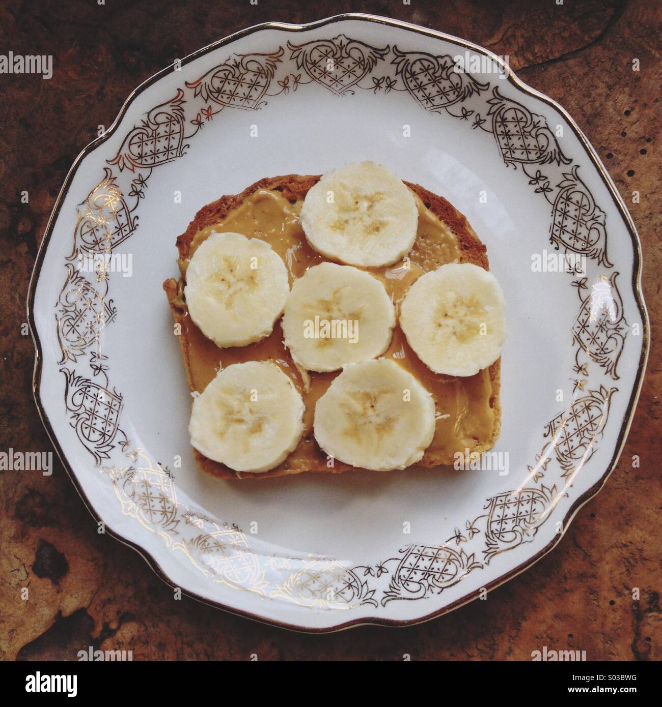 Offenen konfrontiert Erdnussbutter und in Scheiben geschnittenen Bananen Sandwich auf Lust auf gold und weißen Porzellanteller auf rustikalen Tisch Stockfoto