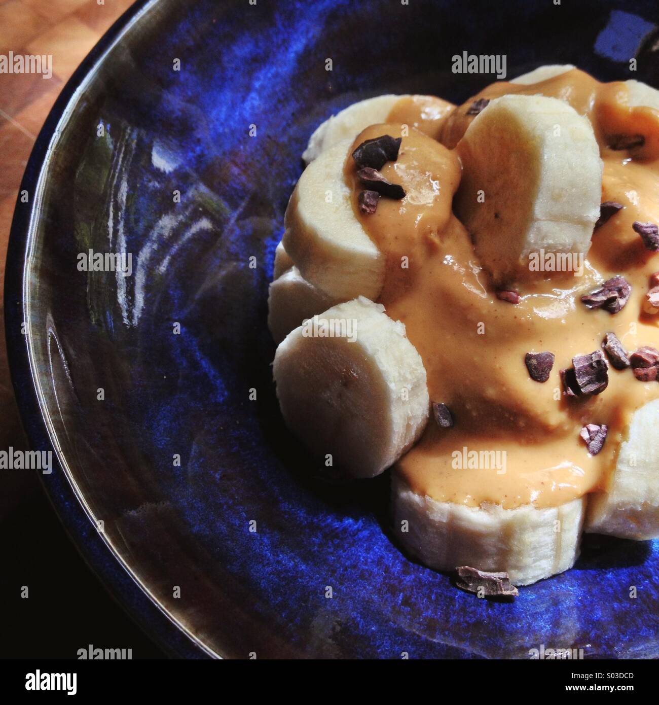 Nahaufnahme von blau glasierte Schale mit Bananenscheiben, Erdnussbutter, Kakaonibs auf Hackstock Stockfoto
