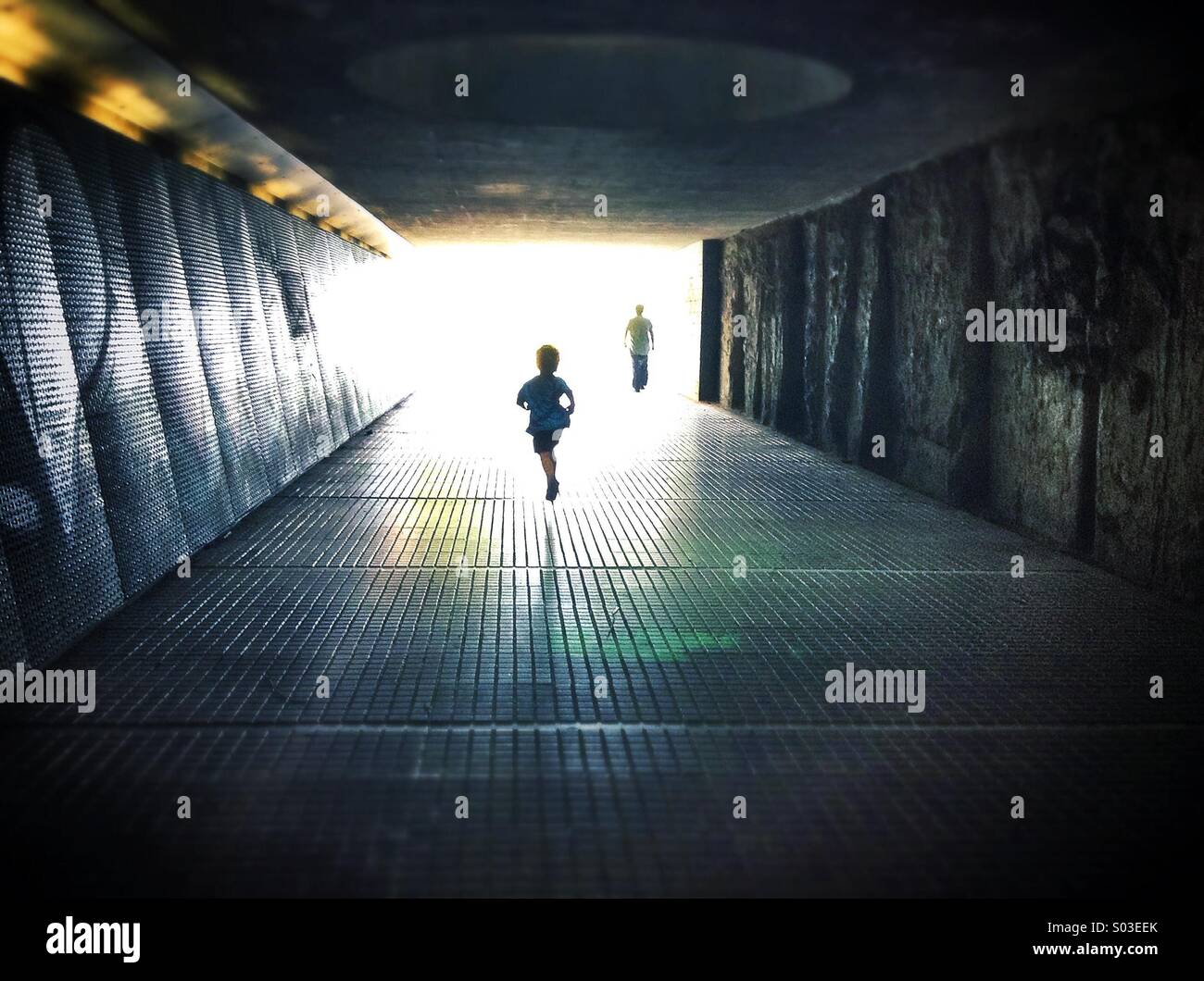 Silhouetten, die zu Fuß durch einen dunklen unter pass Säule Licht am Ende des Tunnels Stockfoto