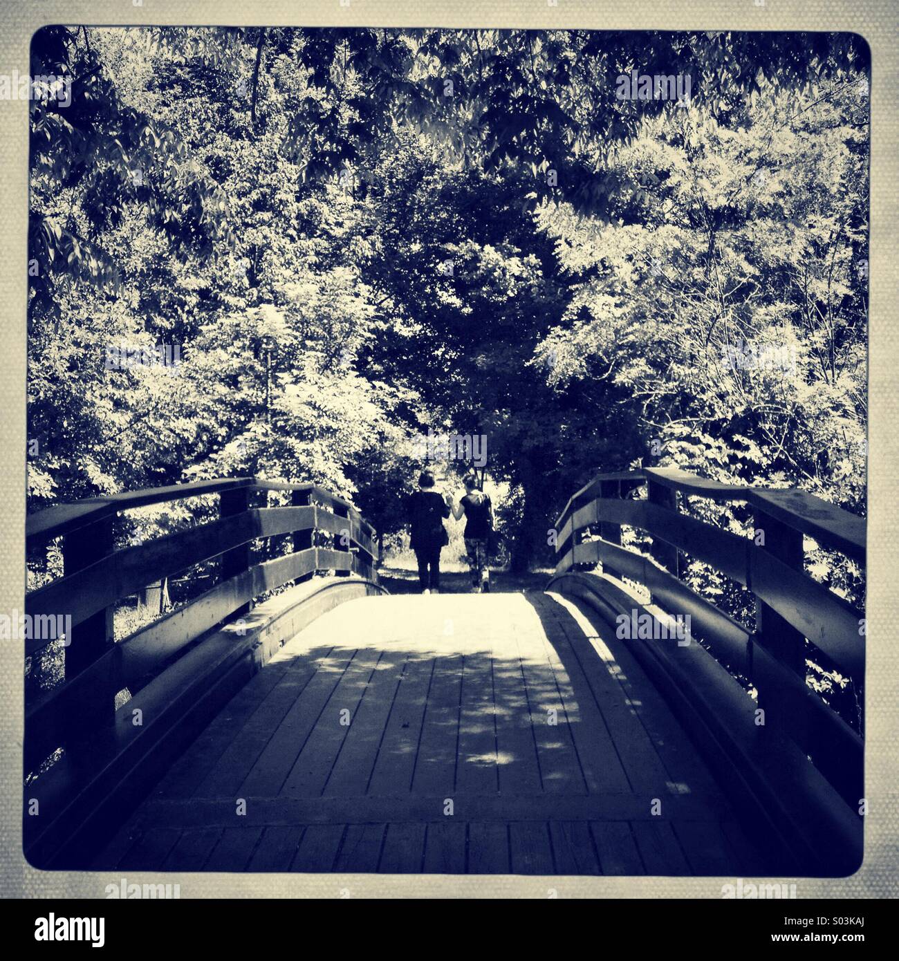 Zwei Freunde, die über eine Brücke in einem Garten, Hand in Hand Stockfoto