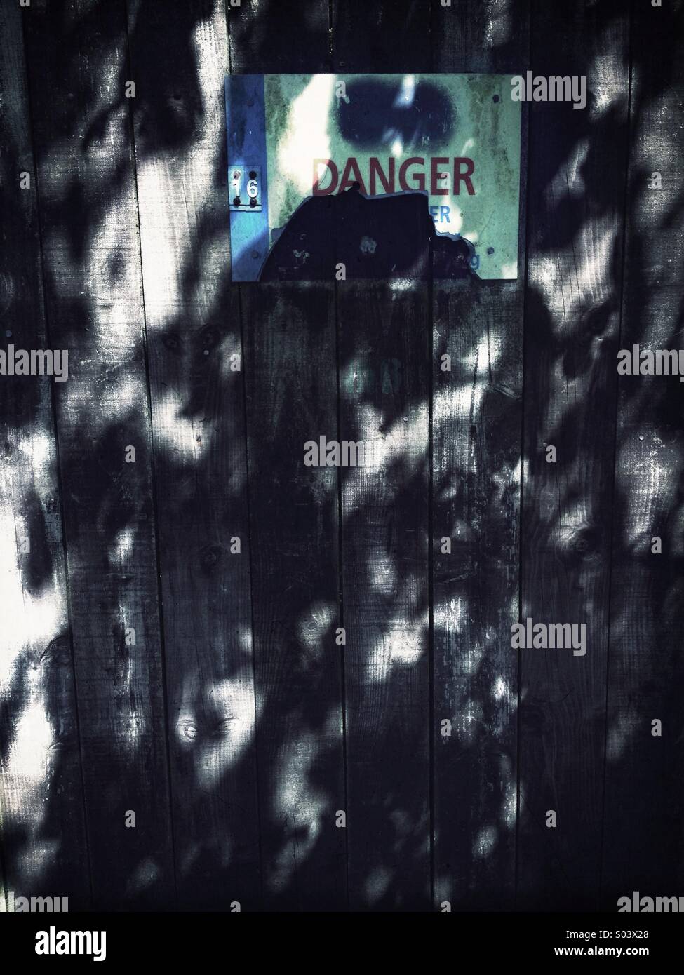 Gefahrenzeichen auf Schatten gefleckten Zaun beschädigt Stockfoto