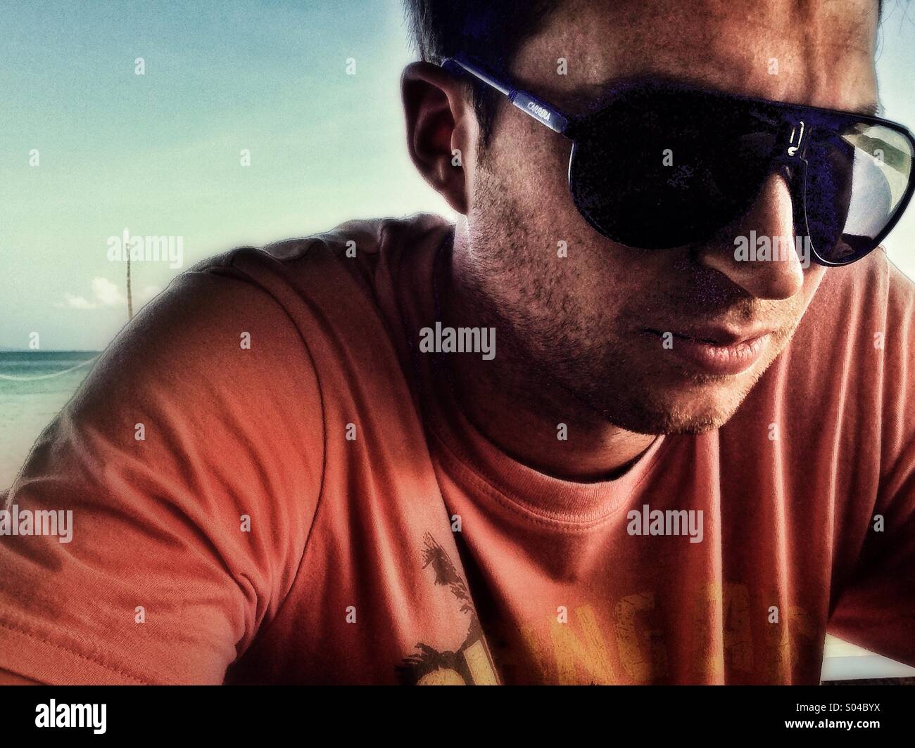 Mann mit orangefarbenen t-Shirt und Sonnenbrille, nachdenklich, Suche Dj am Strand Stockfoto