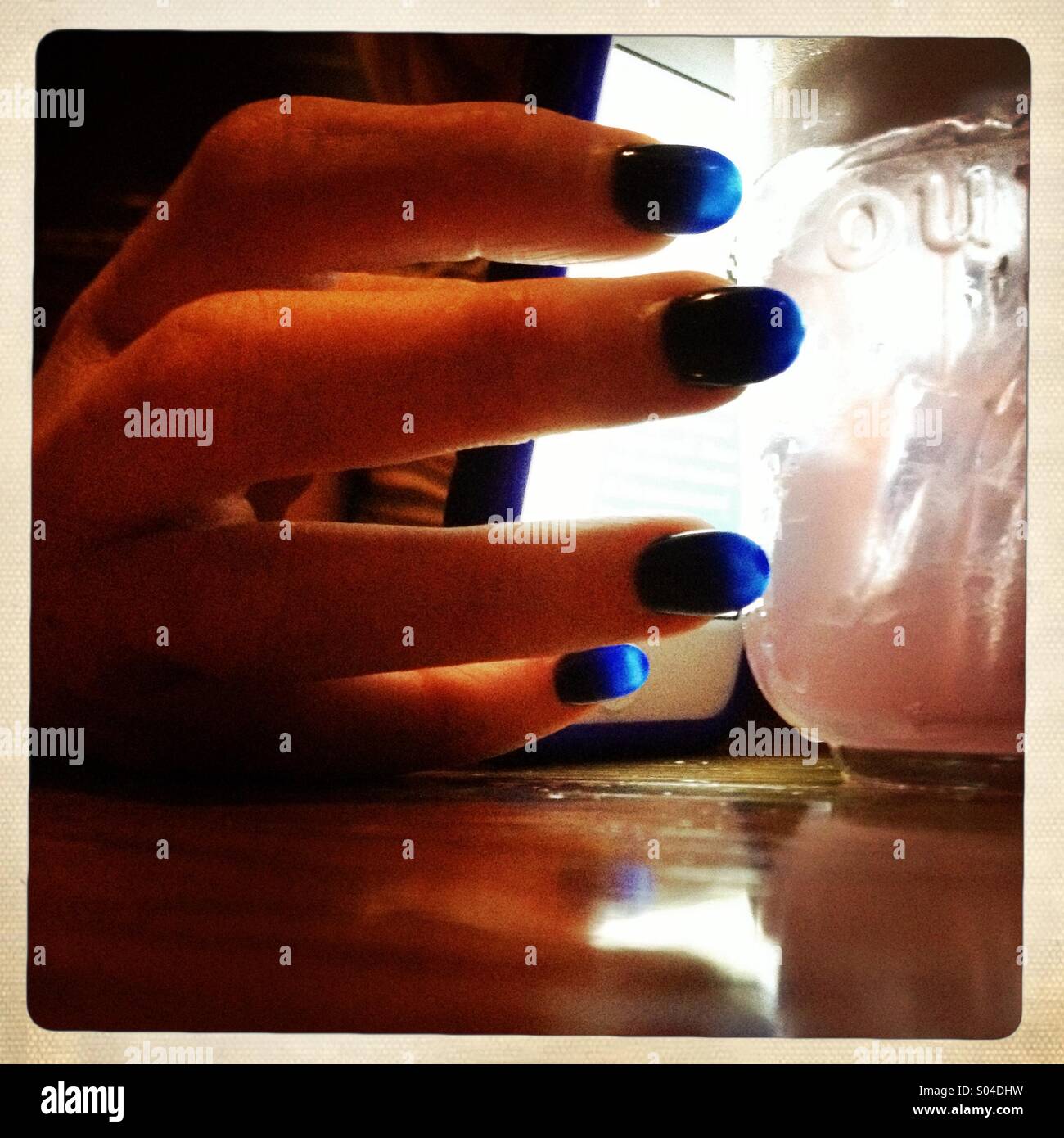 Eine Dame Blaue Fingernägel glühen aus einer Lichtquelle durch ein Glas Wasser Stockfoto