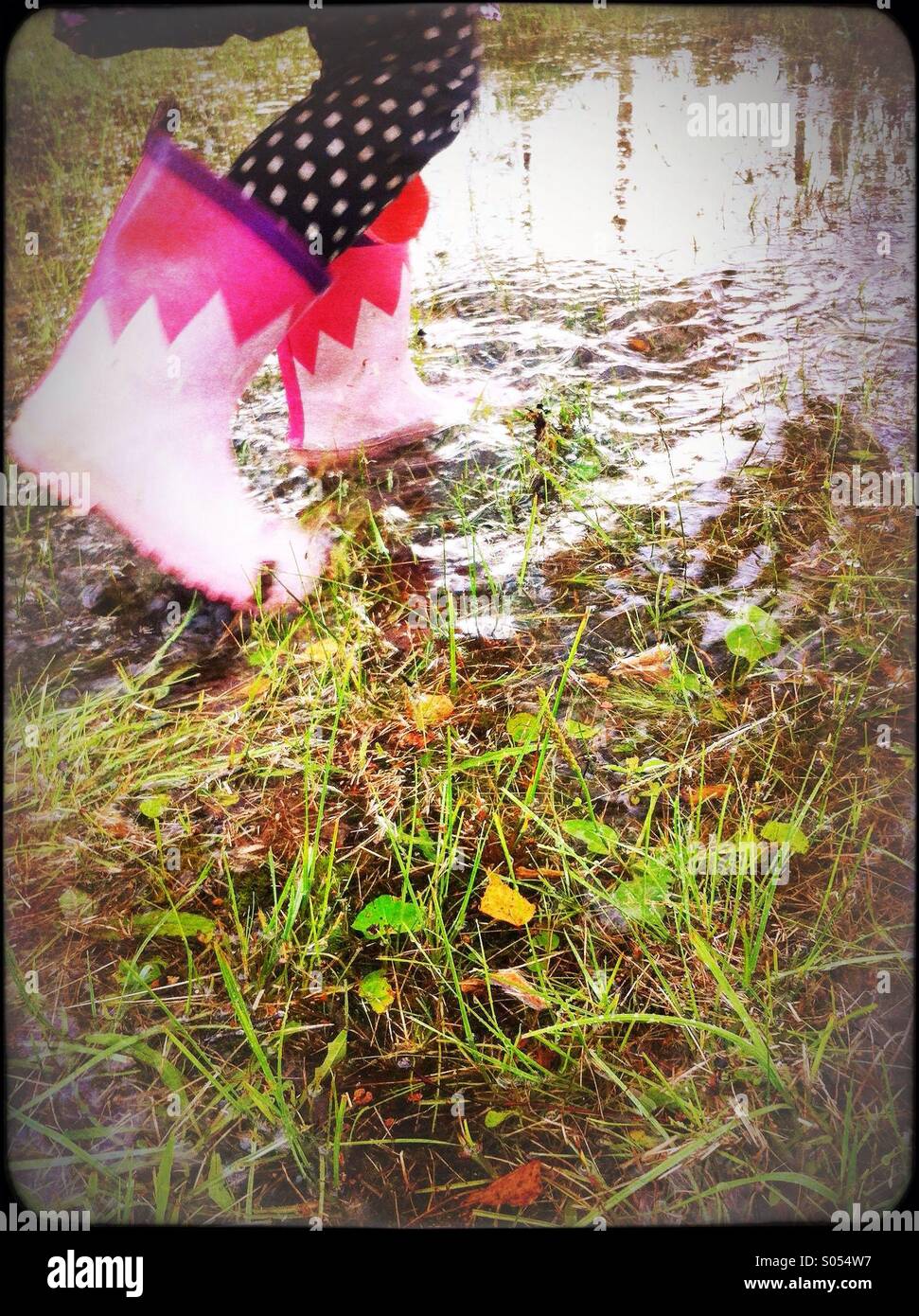 Ein Mädchen zu Fuß auf einem Teich mit rosa Gummistiefeln Stockfoto