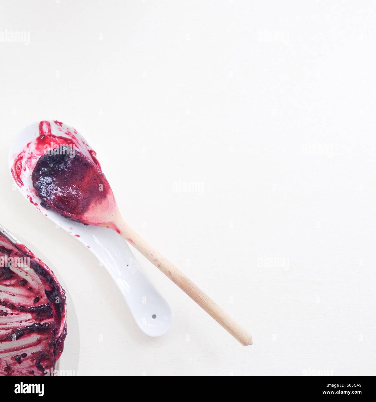 Holzlöffel auf Löffel Rest und Topf verschmiert mit Brombeermarmelade auf weißem Hintergrund Stockfoto