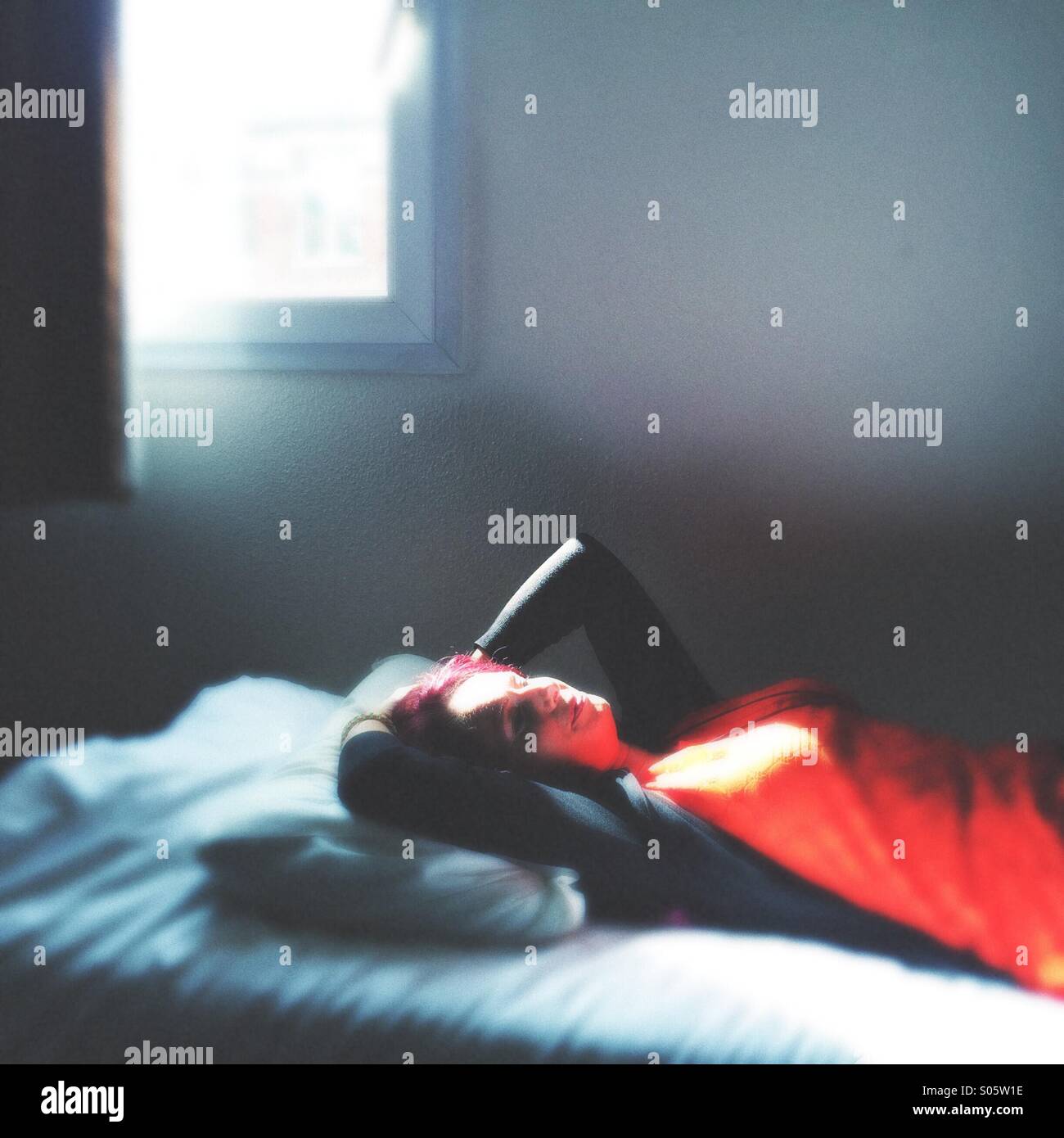 Frau in einem roten Kleid auf einem Bett liegend, Nachmittag Stockfoto
