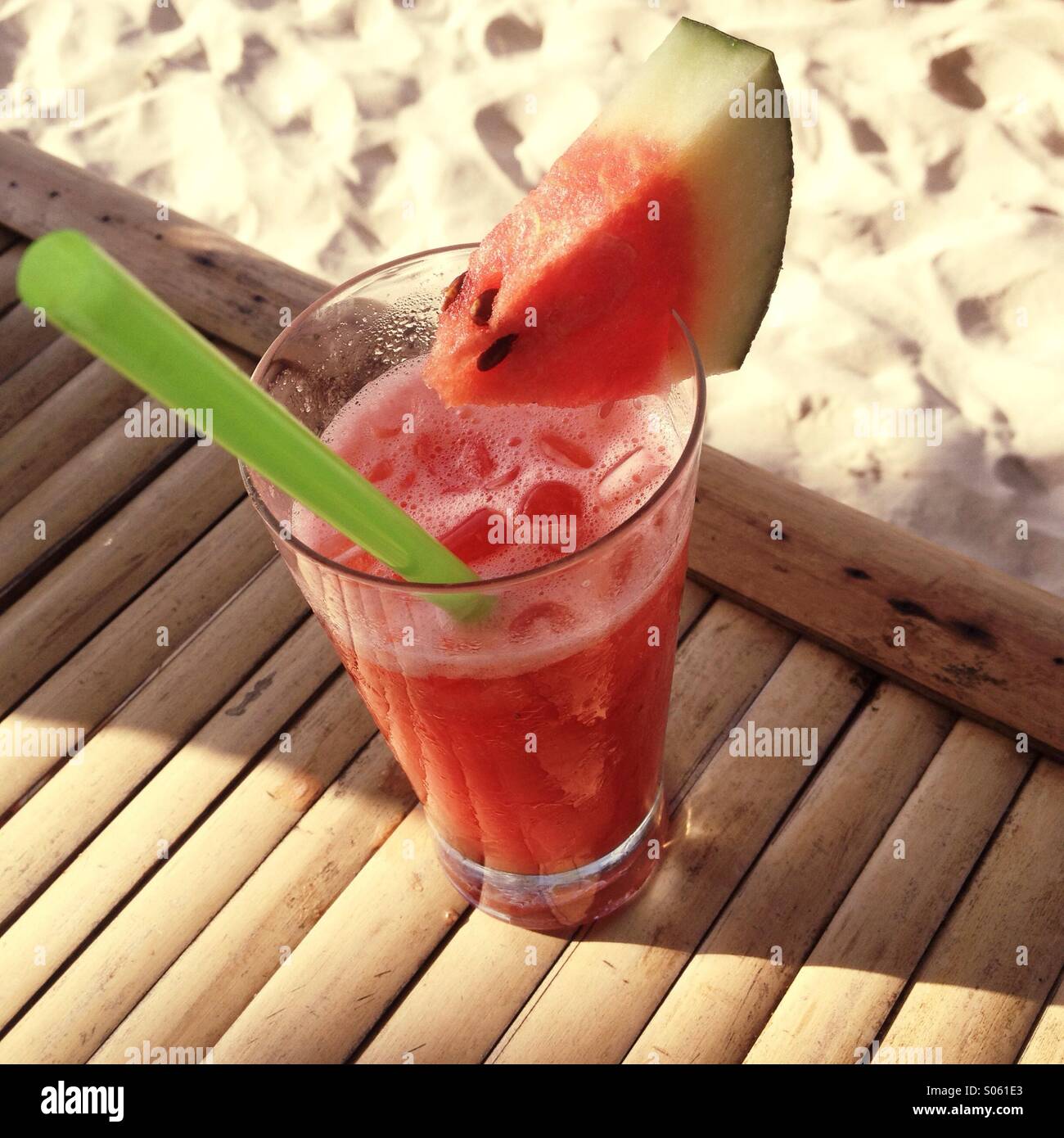 Kombinierte tropischen Drink mit Eis, Wassermelone Keil und Stroh in der Sonne auf Bambus-Tisch am Strand in Thailand. Stockfoto