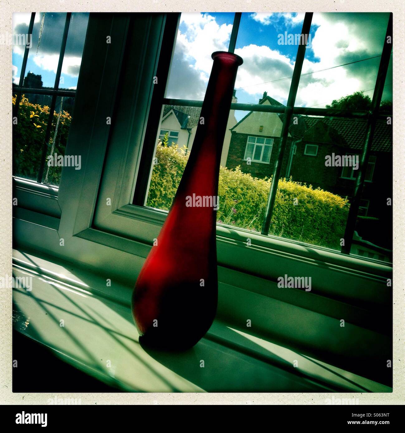 Eine rote Glasvase auf der Fensterbank an einem sonnigen Tag Stockfoto