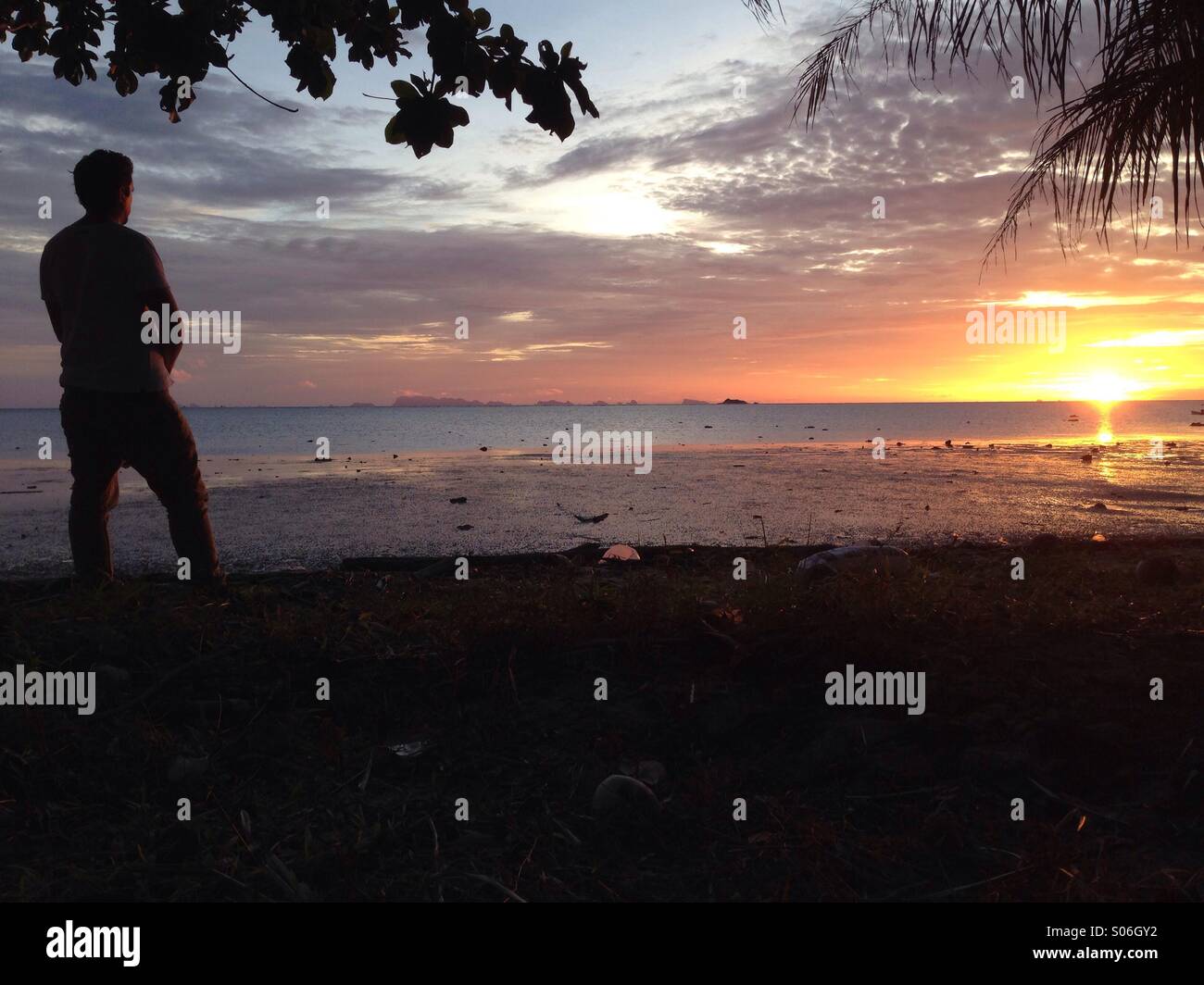 Solo-Reisenden einen tropischen Sonnenuntergang unter einer Palme am Strand Stockfoto