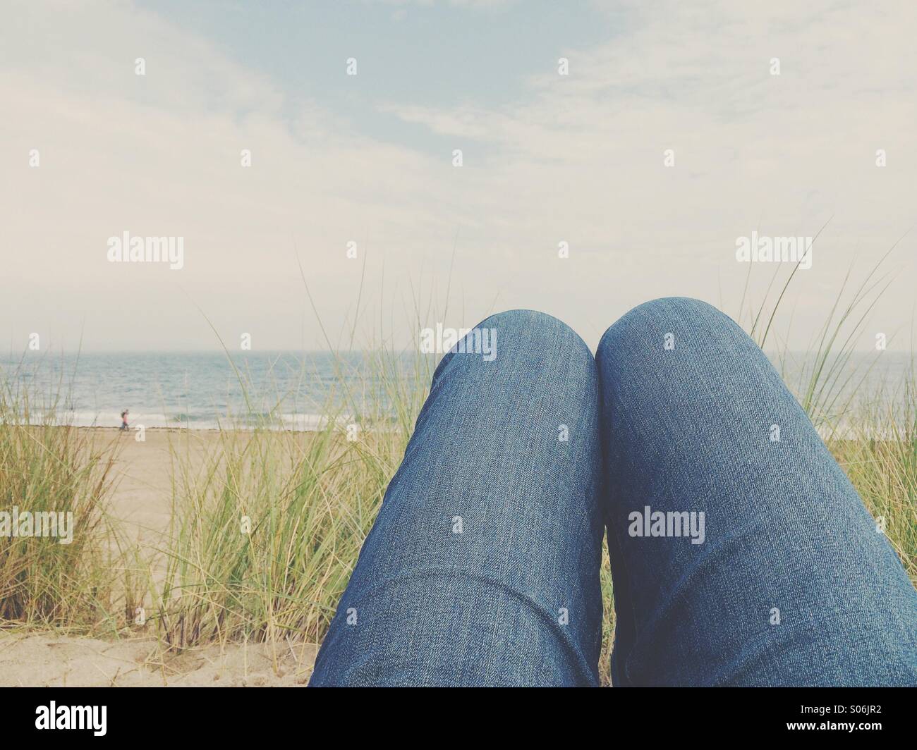 Knie der Person, die in den Dünen mit dem Strand als liegt Ein Hintergrund Stockfoto