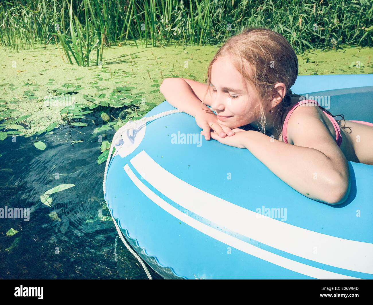 Kleines Mädchen sitzt in einem Floß auf einem Fluss mit üppigem Grün Stockfoto