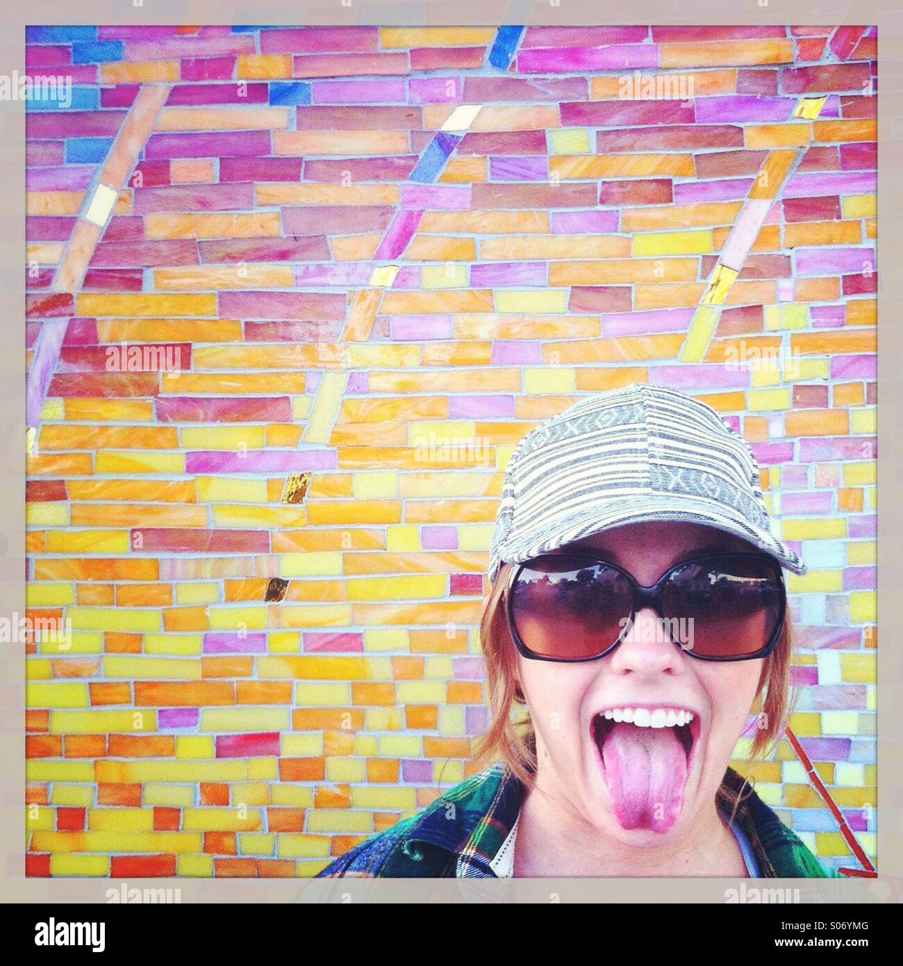 Frau, die ihre Zunge vor Mosaikwand Stockfoto