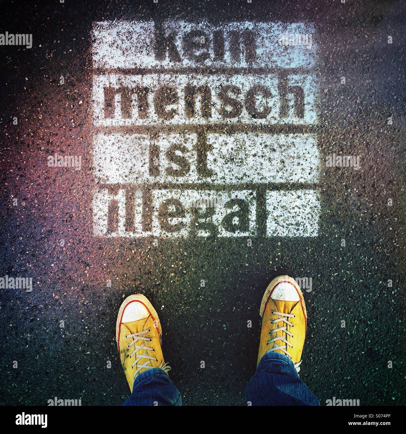 Person, die Füße neben gesprüht Graffiti auf Bürgersteig mit Worten "Kein Mensch ist Illegal" in deutscher Sprache (kein Mensch ist Illegal) Stockfoto