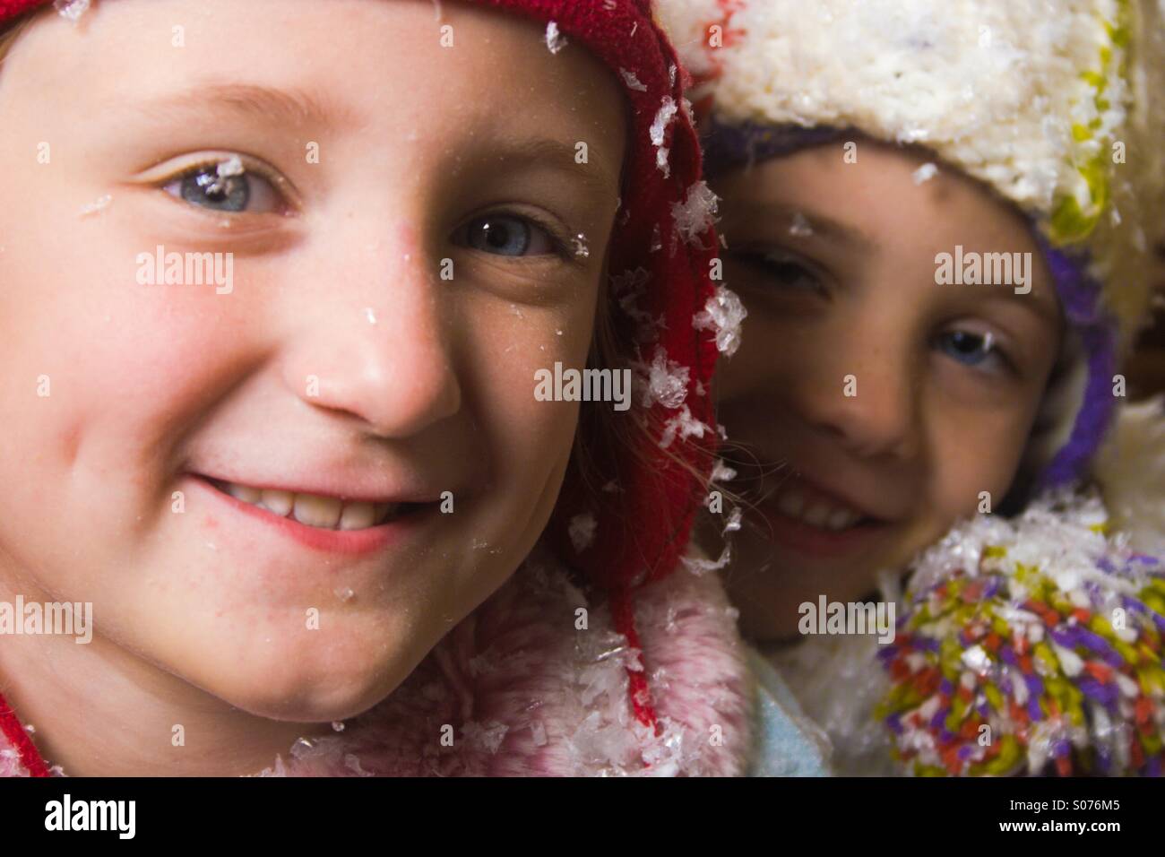 Zwei 6-jährige Mädchen in wolligen Mützen im Schnee Stockfoto