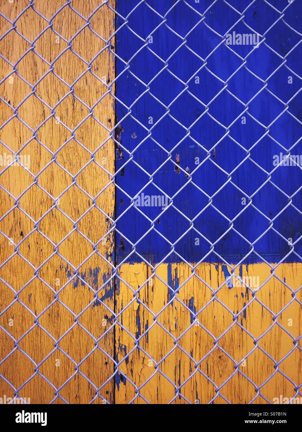 Gelbe und blaue abstrakte urban Texturen. Lackierten Holzplatten hinter einem Maschendrahtzaun. Stockfoto