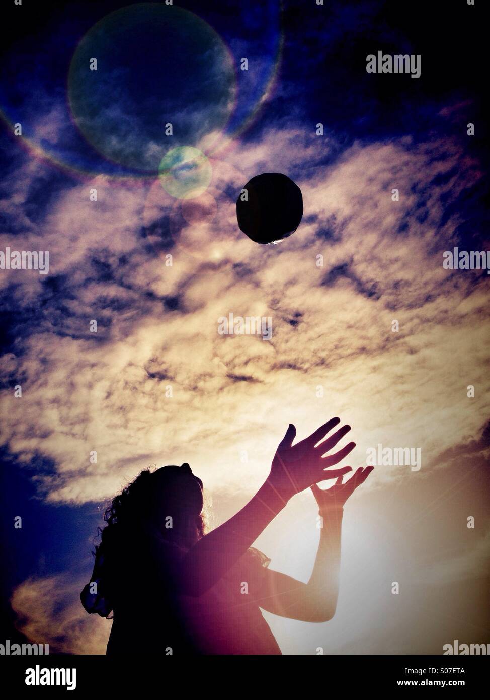 Junges Mädchen wirft Ball in der Luft Hintergrundbeleuchtung durch Sonne Stockfoto