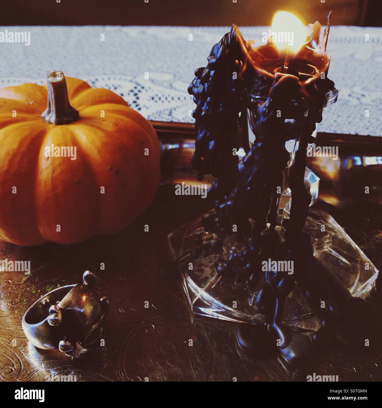 Halloween-Stillleben mit kleiner Kürbis, schwarzen tropfende Kerzen, Totenkopfring am Silbertablett. Stockfoto