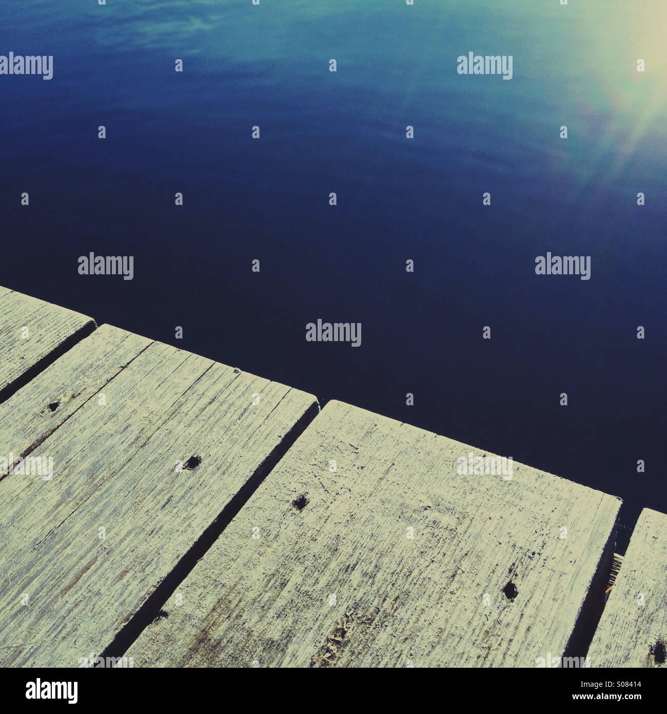 Minimalistische Nahaufnahme von Wasser reflektiert Sonnenlicht am Rand eines Docks. Stockfoto