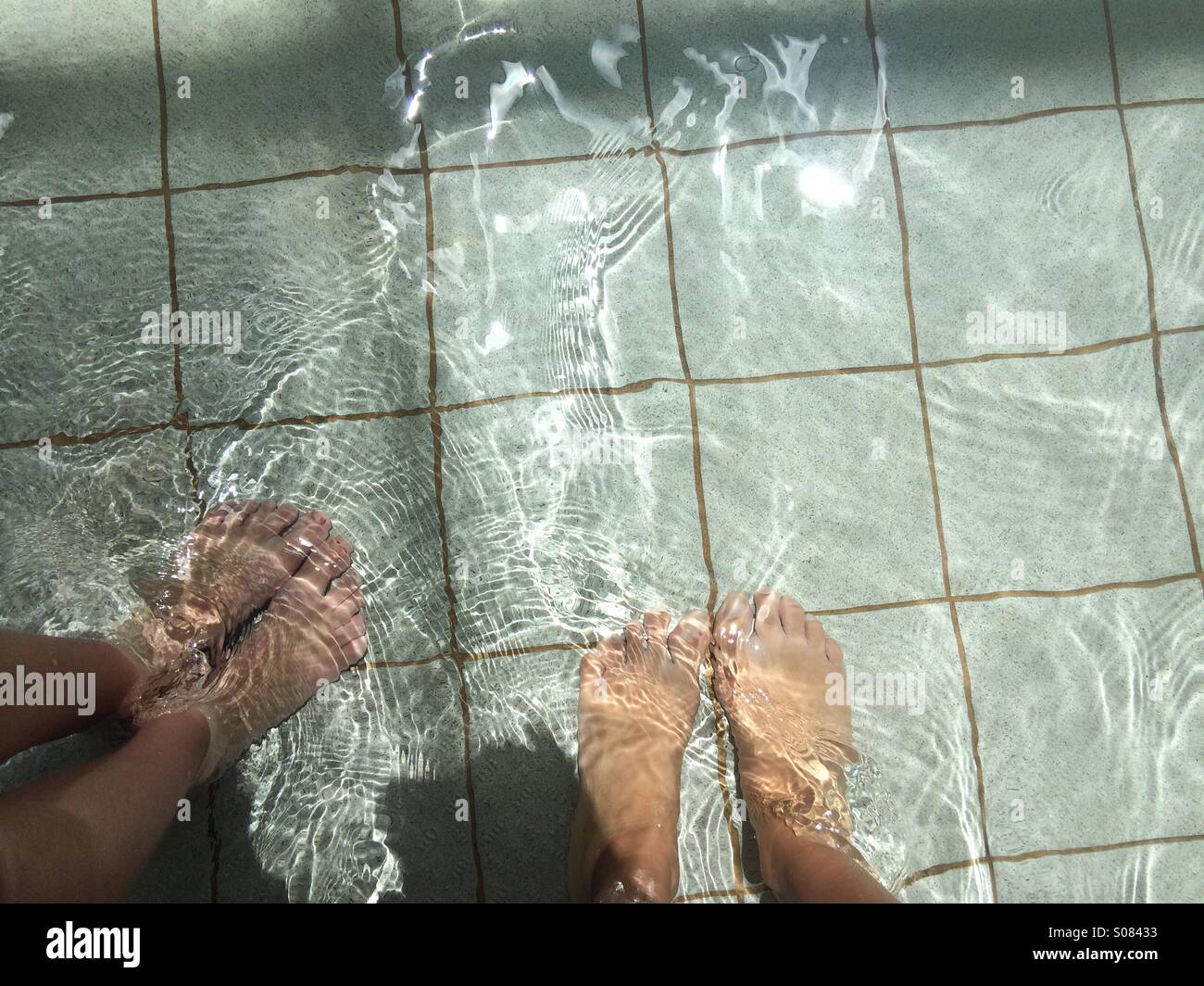 Erste Person POV Mutter und Töchter Füße Paddeln im flachen Pool. Stockfoto