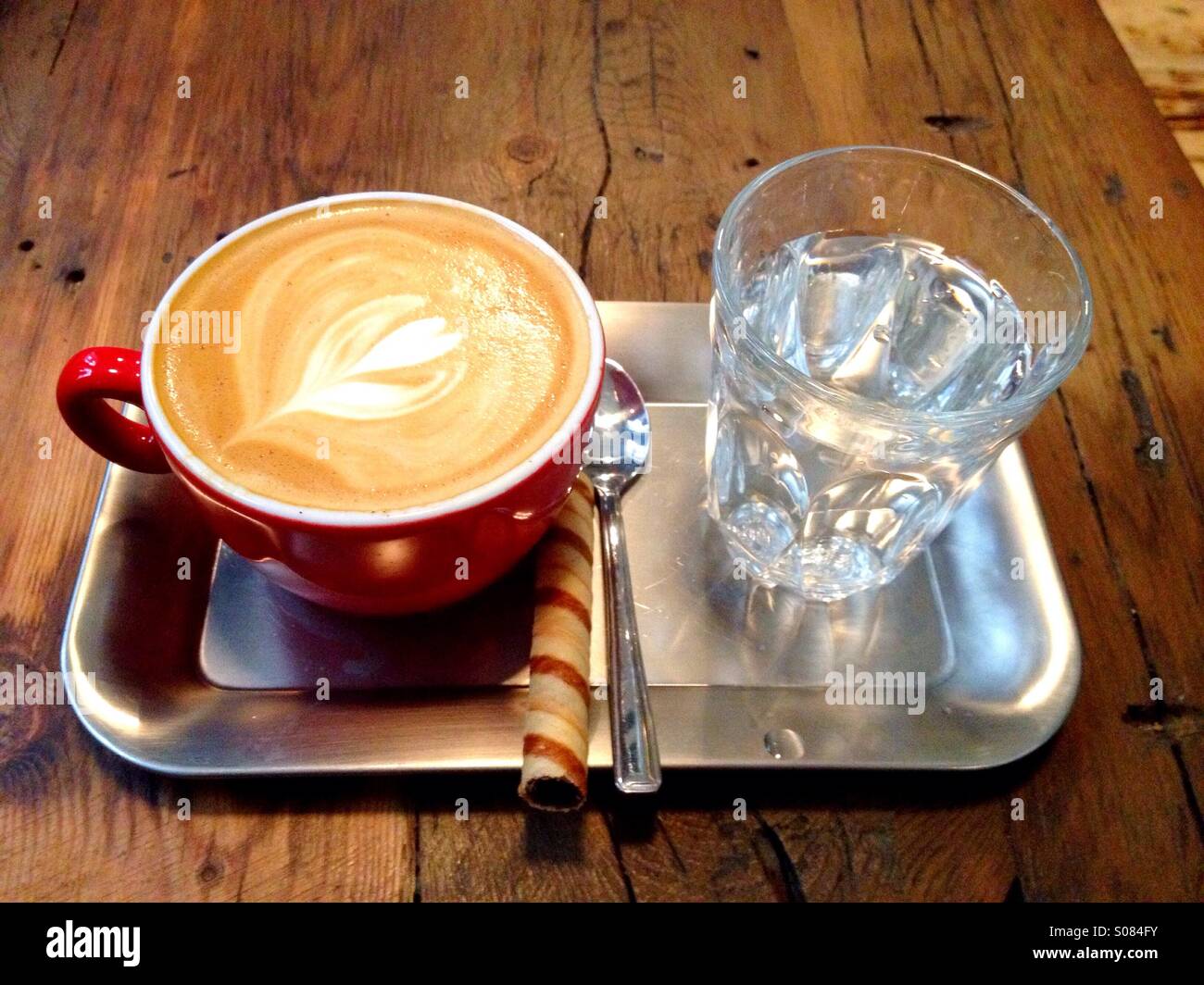 Flache weiße Kaffee in eine rote Tasse auf einem silbernen Tablett auf einem Holztisch Stockfoto