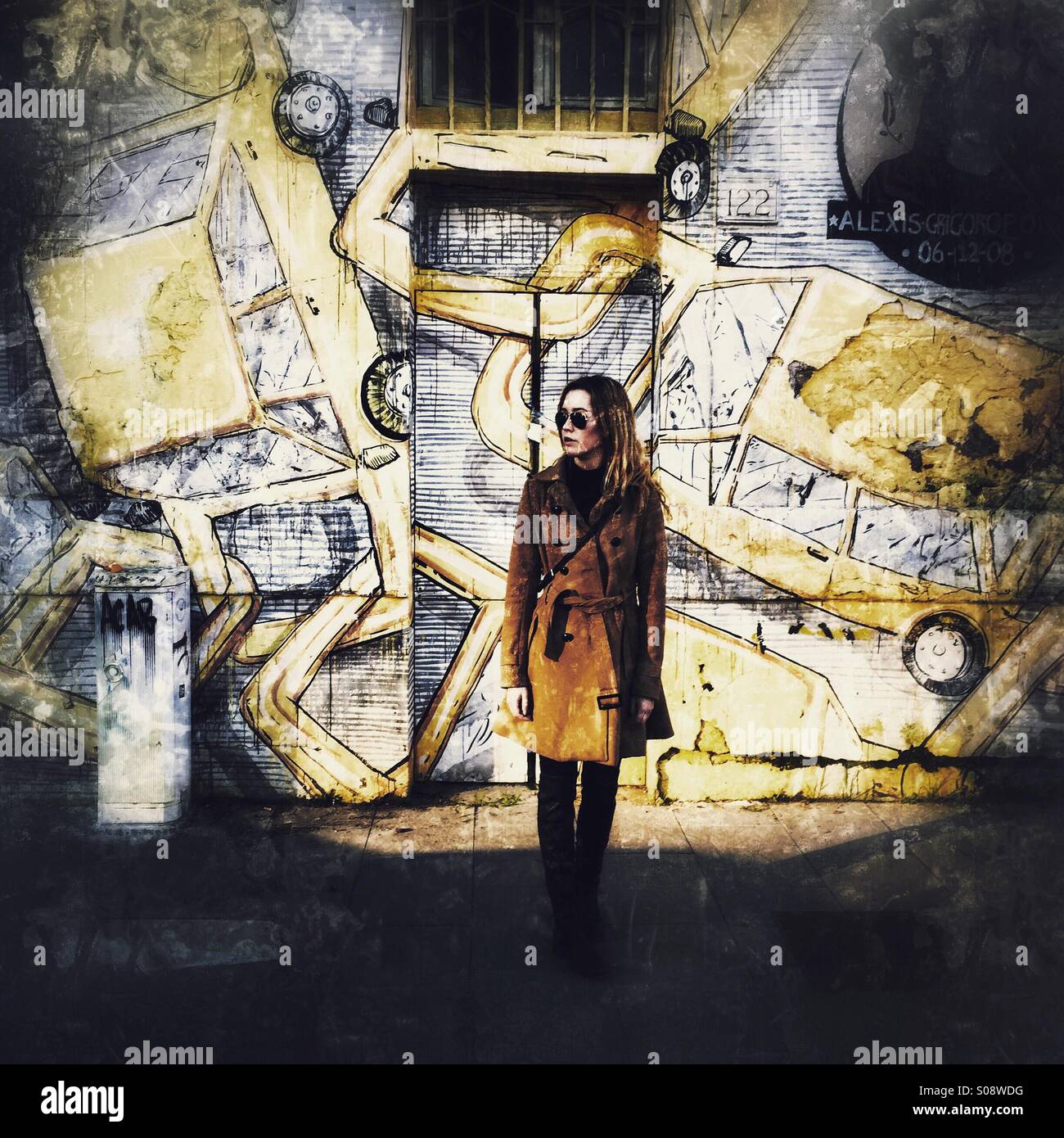 Eine junge Frau stand vor einer Wand mit einem Wandbild des gelben Autos. - Smartphone-aufgenommenes Stockfoto