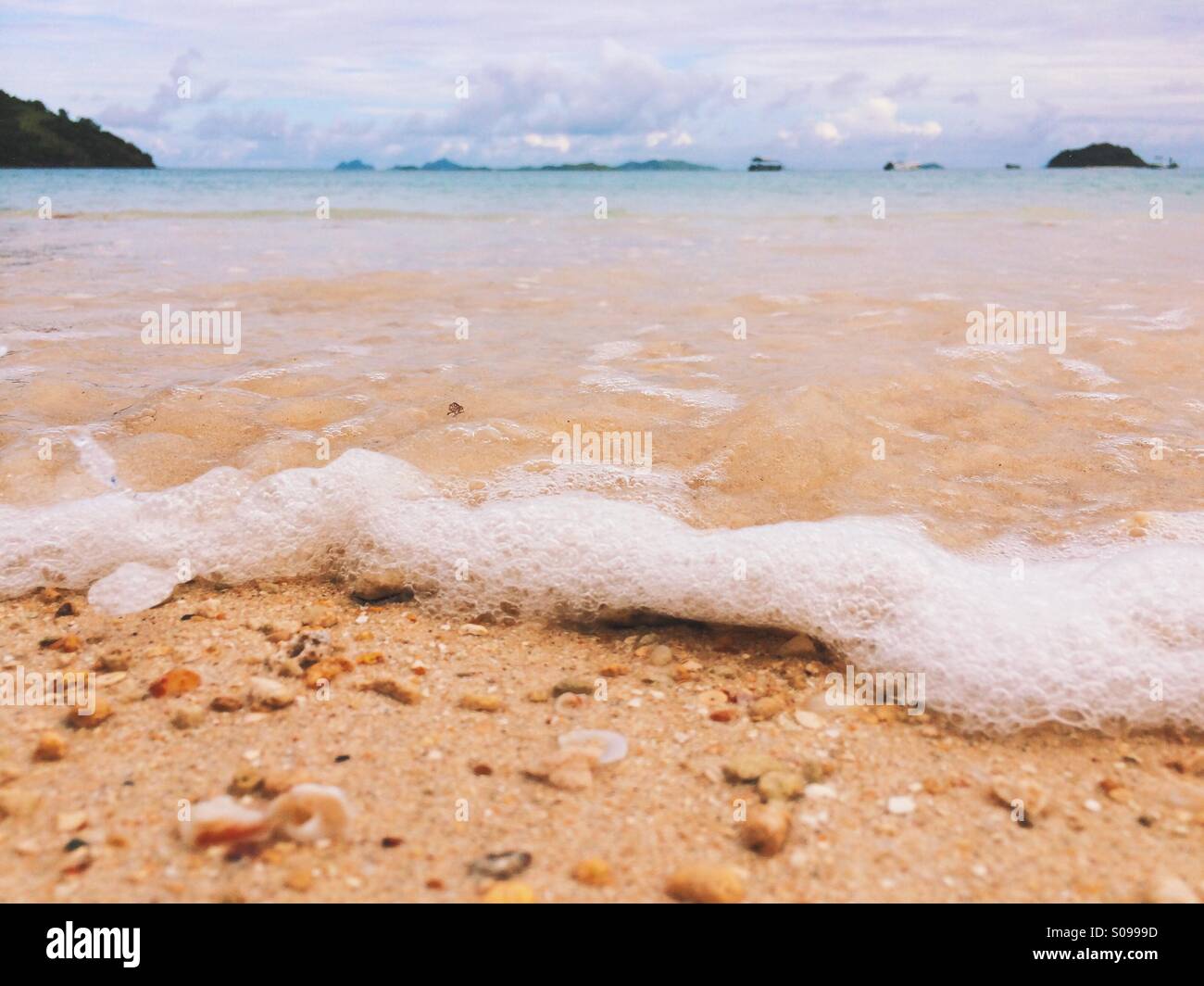 Nahaufnahme der sprudelnde Wellen am Sandstrand mit Inseln im Hintergrund. Stockfoto