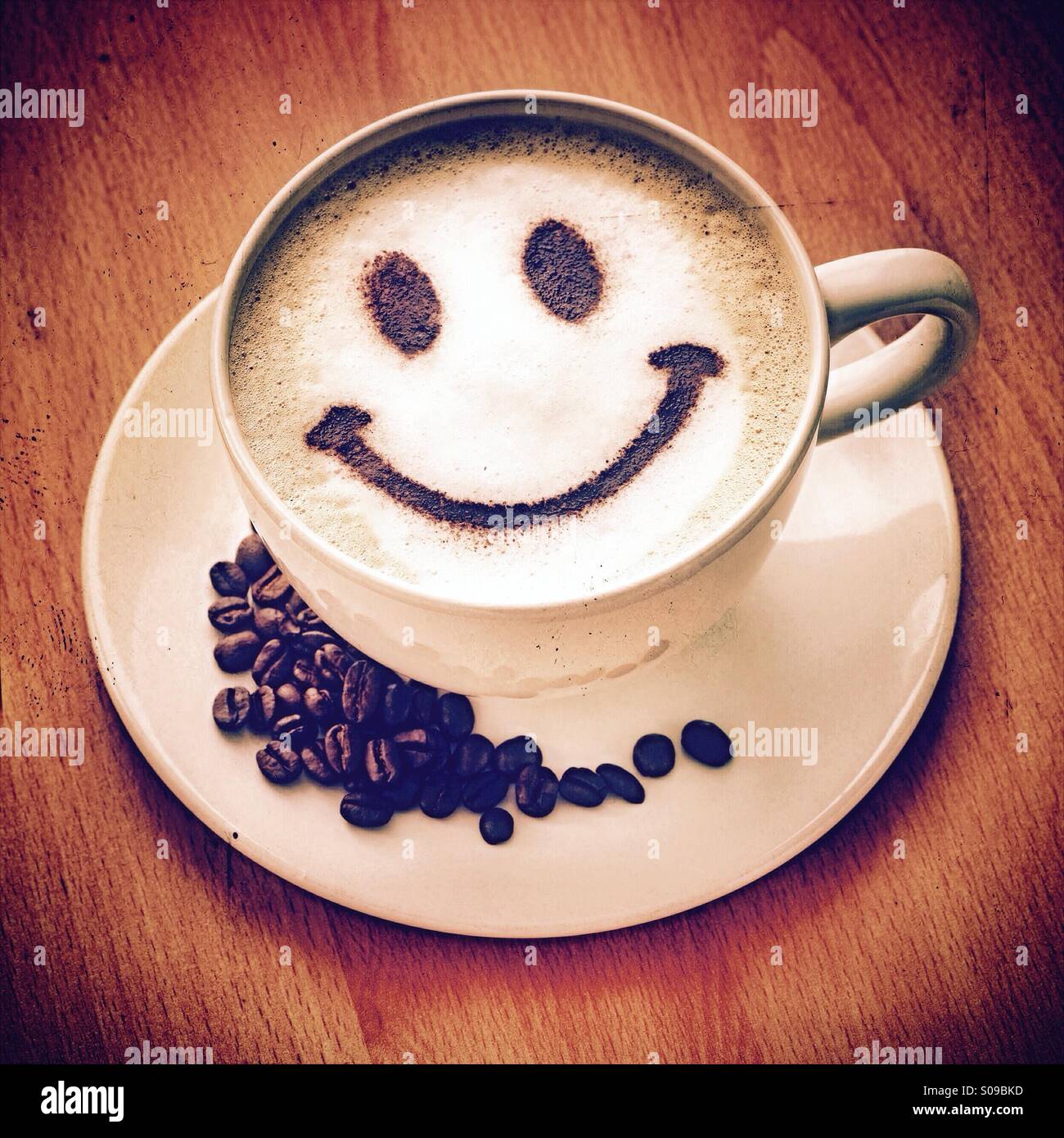 Kaffeepause - ein Cappuccino mit einem Schokoladenpulver Smiley und Kaffeebohnen auf der Untertasse Stockfoto