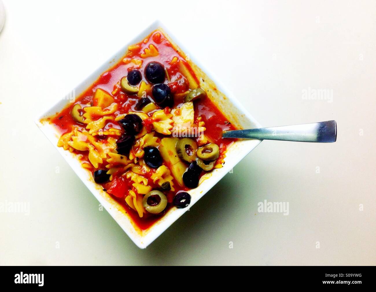 Vegane Bio Tomatensuppe mit Bogen Nudeln und Oliven in eine quadratische weiße Schale Stockfoto
