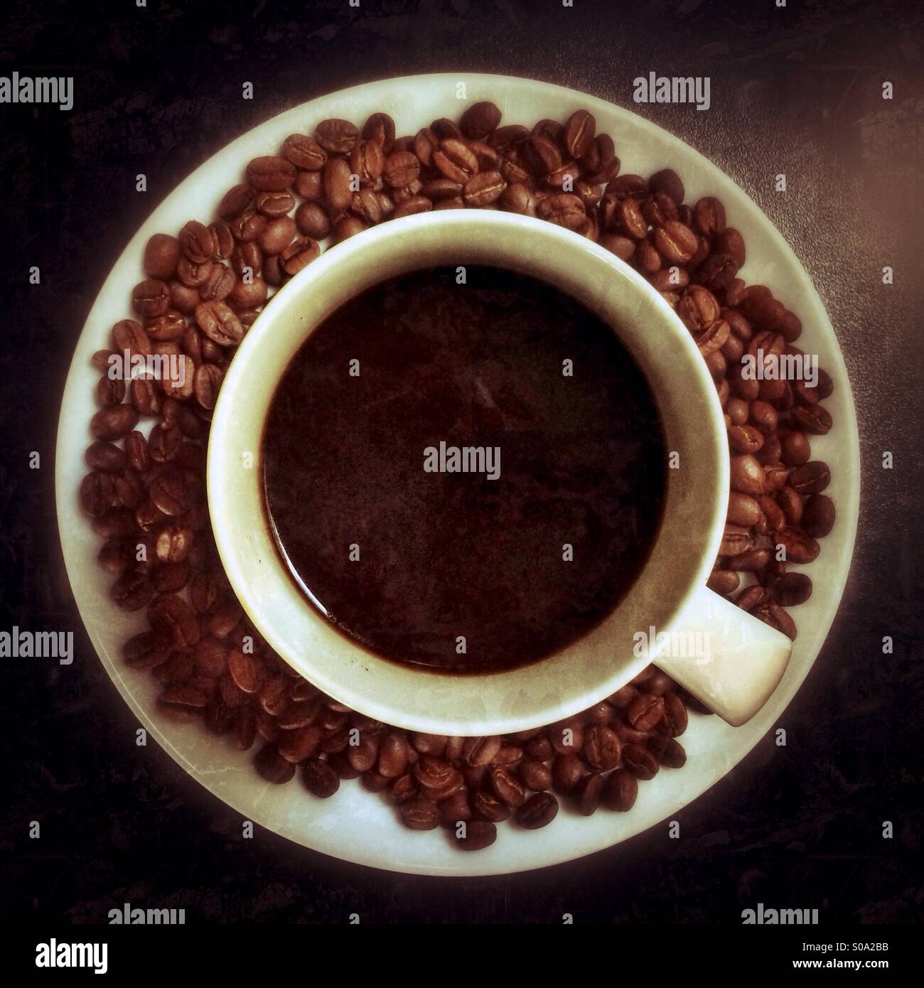 Eine Tasse schwarzen Kaffee und Kaffeebohnen auf einem weißen Teller, von oben gesehen. Stockfoto