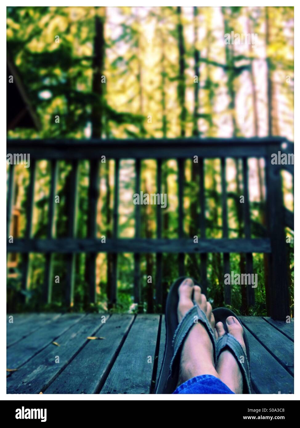 Ein Mann Füße gekreuzt sitzend auf einem Holzdeck auf einen Wald. Stockfoto