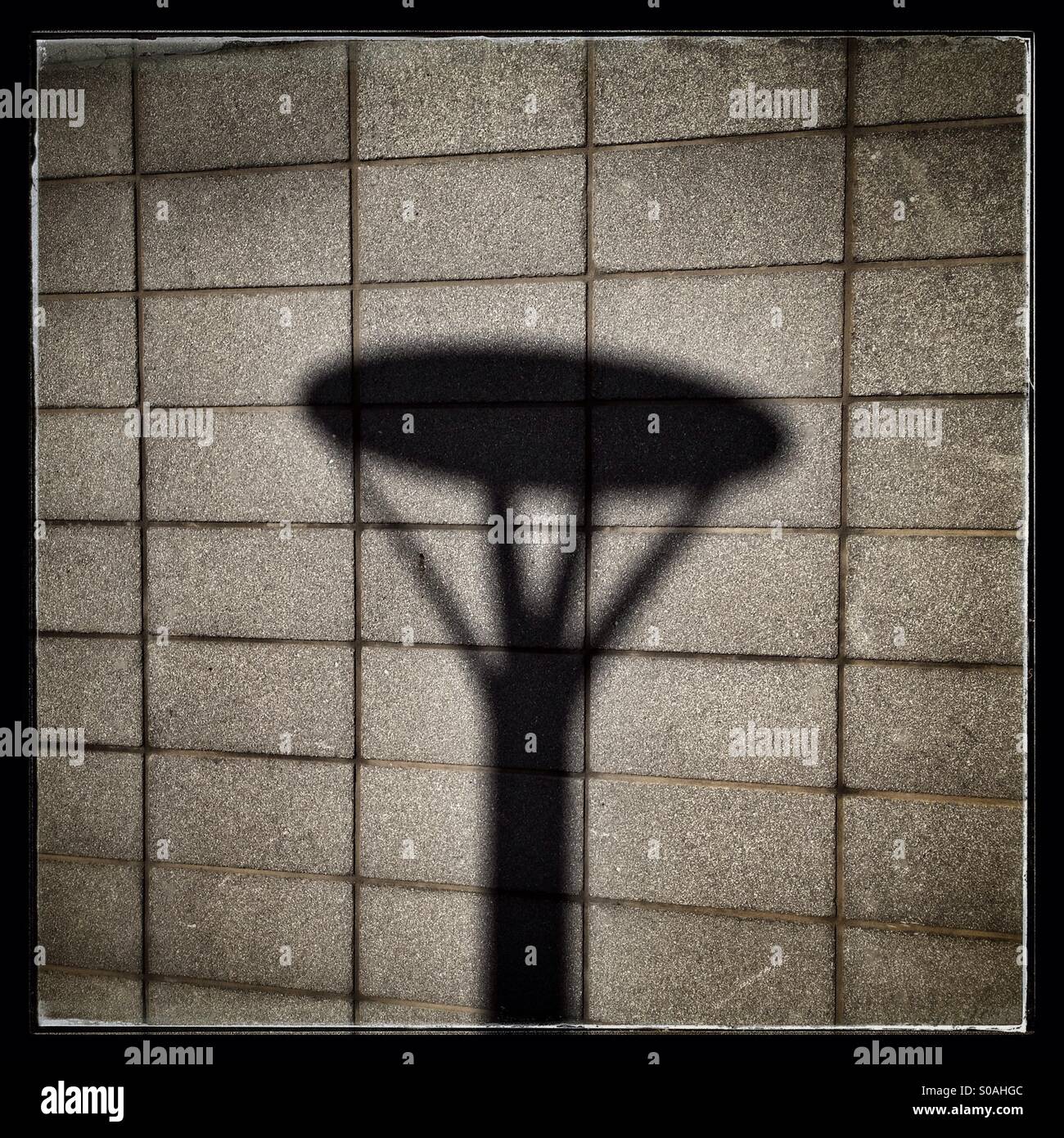Schatten einer Straßenlaterne gegen das rechteckige Muster an der Wand eines Gebäudes. - Smartphone-aufgenommenes Stockfoto