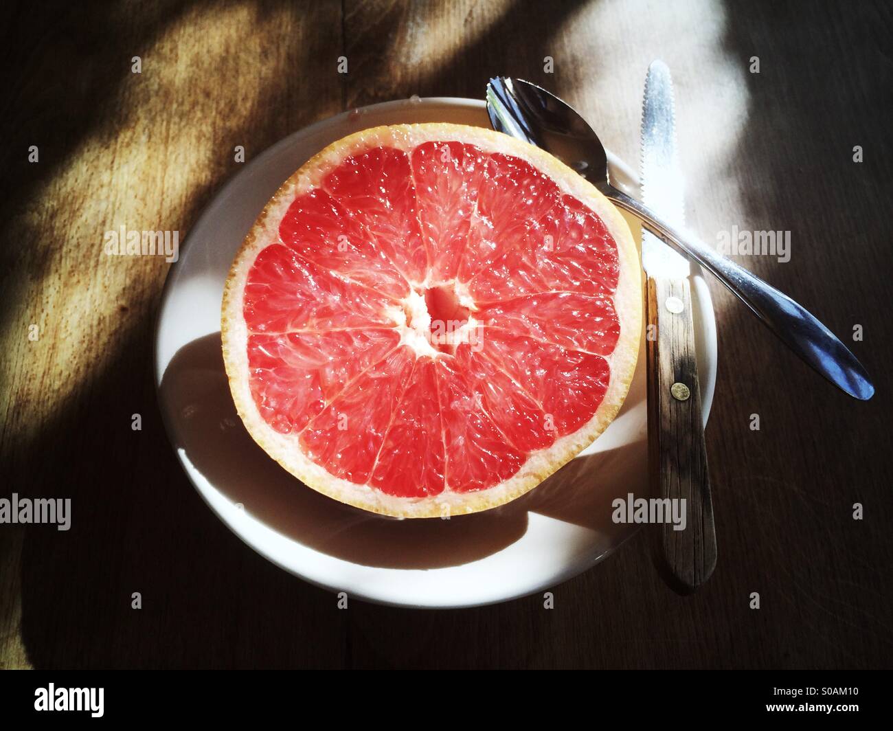 Eine rote Grapefruit halbieren in einer Schüssel mit einem Löffel Grapefruit und einem Grapefruit-Messer auf einem Holztisch. Stockfoto