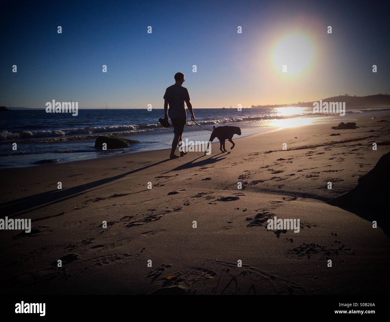 Mann geht seinen Hund bei Sonnenuntergang am East Beach, Santa Barbara, Kalifornien Stockfoto