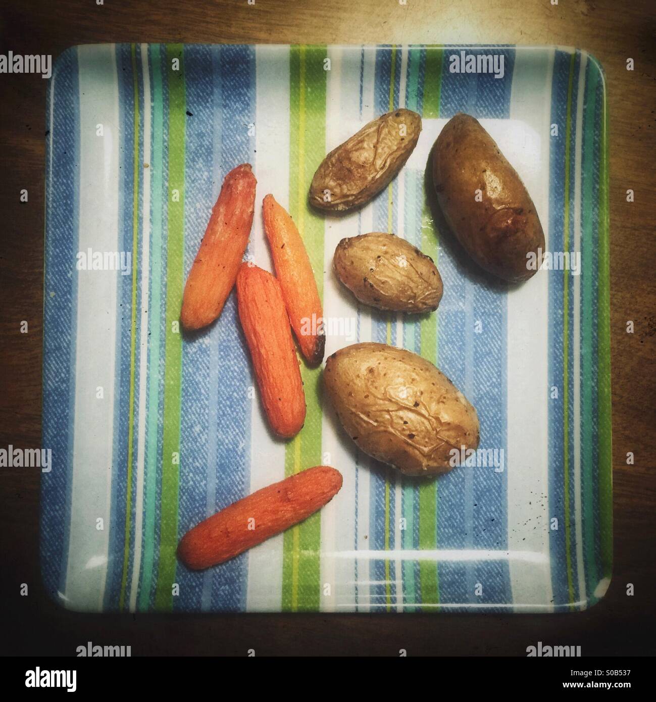 Geröstete Fingerling Kartoffeln und Karotten auf einem gestreiften Teller Stockfoto