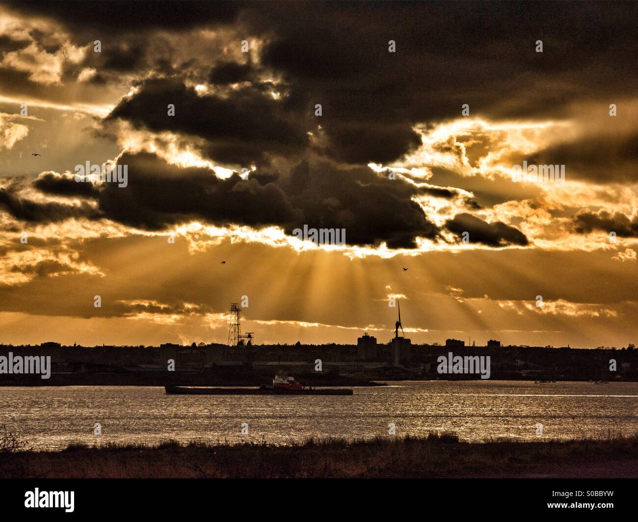 Ein Schiff fährt auf dem Fluss Themse bei Rainham Marshes, Essex, England in einen spektakulären Sonnenuntergang. Stockfoto