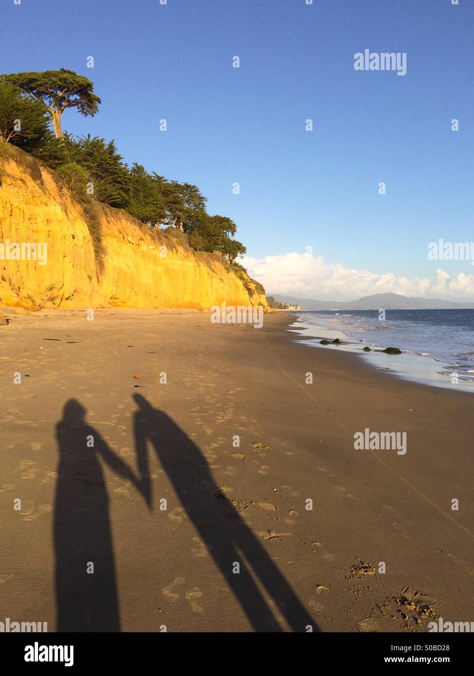 Schatten einer Frau und Mann Hand in Hand im Butterfly Beach in Montecito, Kalifornien - Smartphone-aufgenommenes Stockfoto