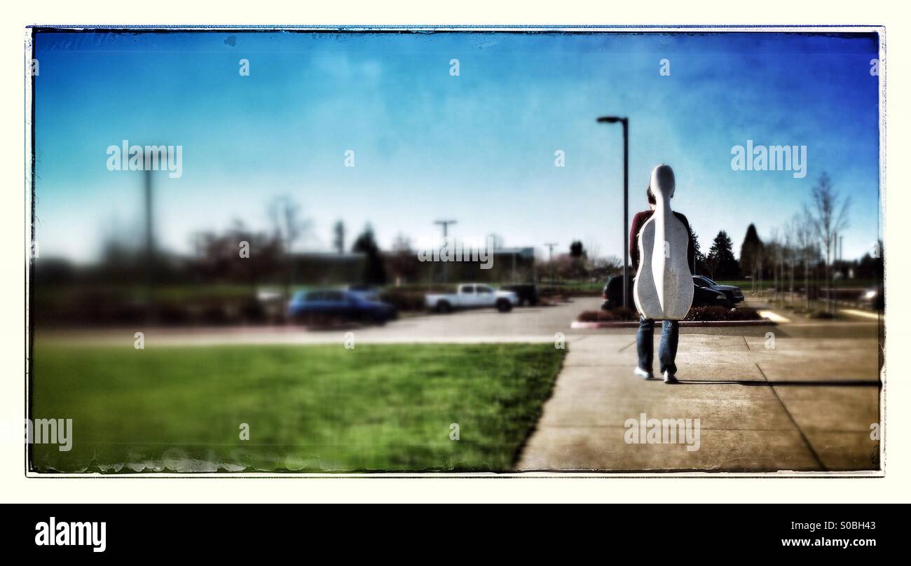 Mann zu Fuß mit dem Cellokasten auf seinem Rücken auf Parkplatz Stockfoto