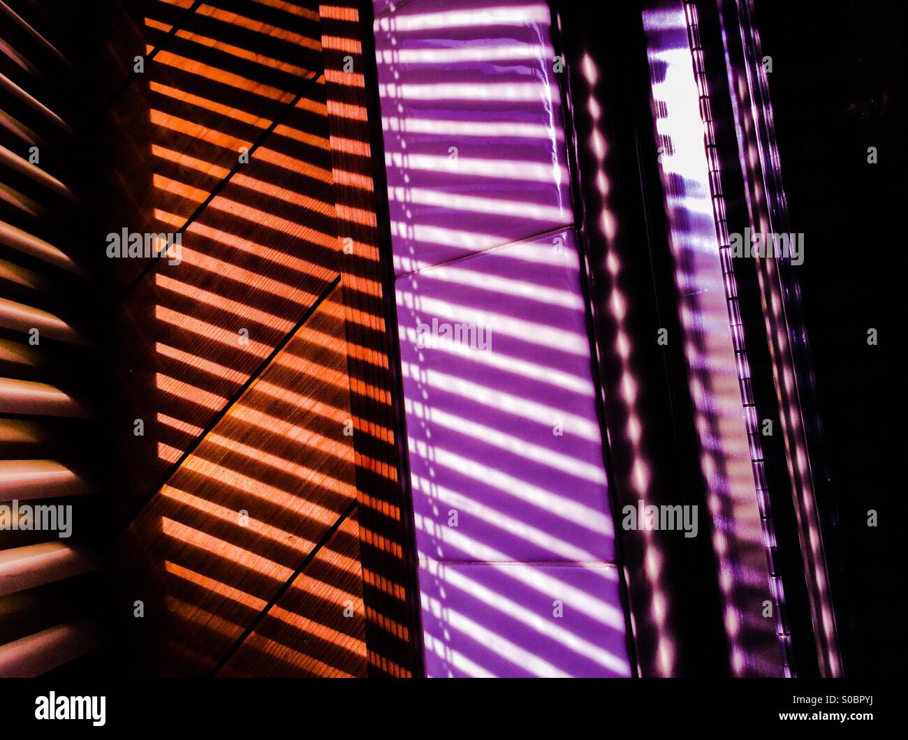 Lichtstrahlen. Fensterläden, die von Lichtern in verschiedenen Farben beleuchtet werden, bilden ein komplexes Muster. Gewinkelte, parallele, geometrische Formen in geraden Linien - Smartphone-aufgenommenes Stockfoto