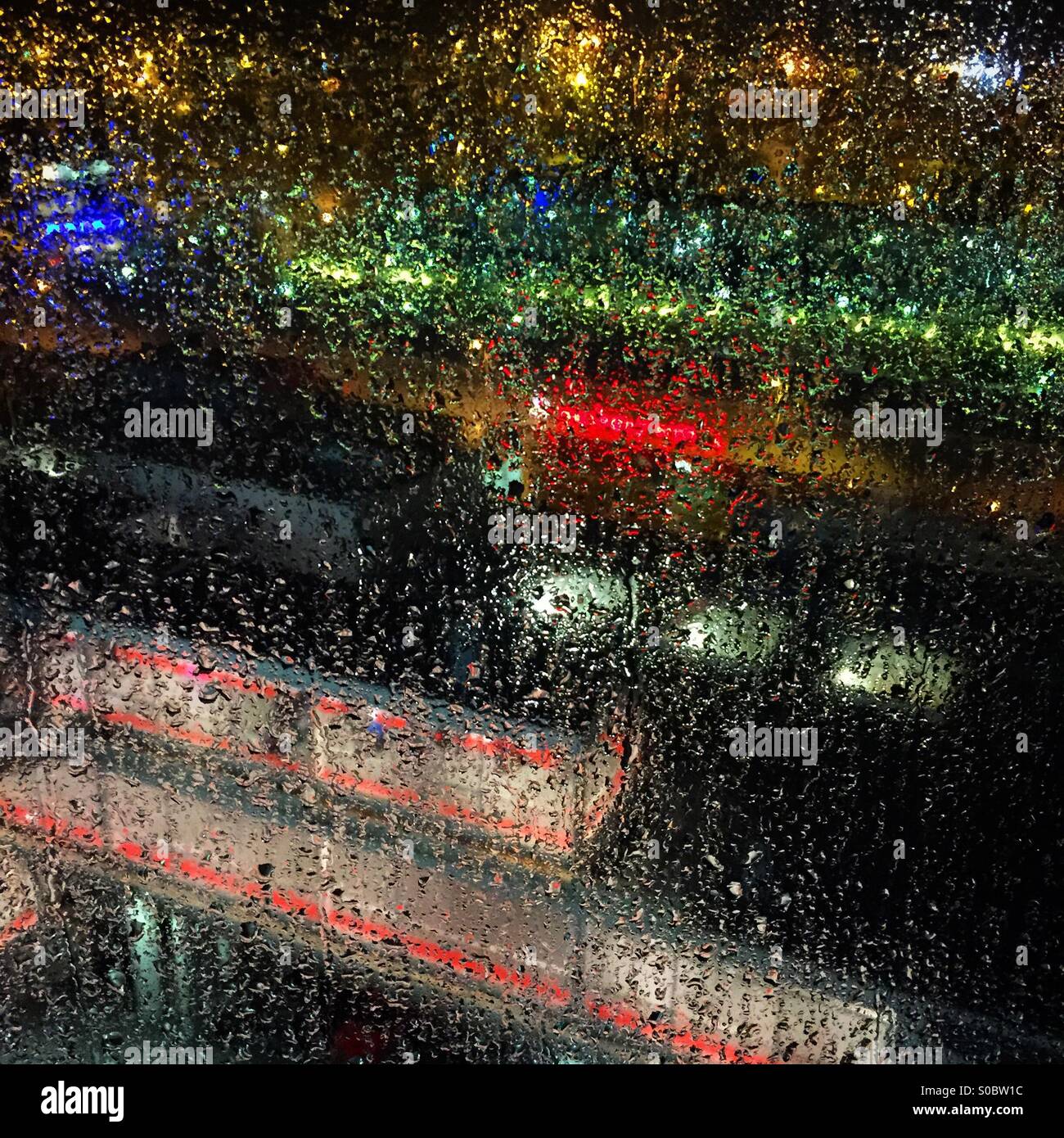 Eine hell erleuchtete Neon Stadt nachts durch einen regnerischen Hotelfenster Stockfoto