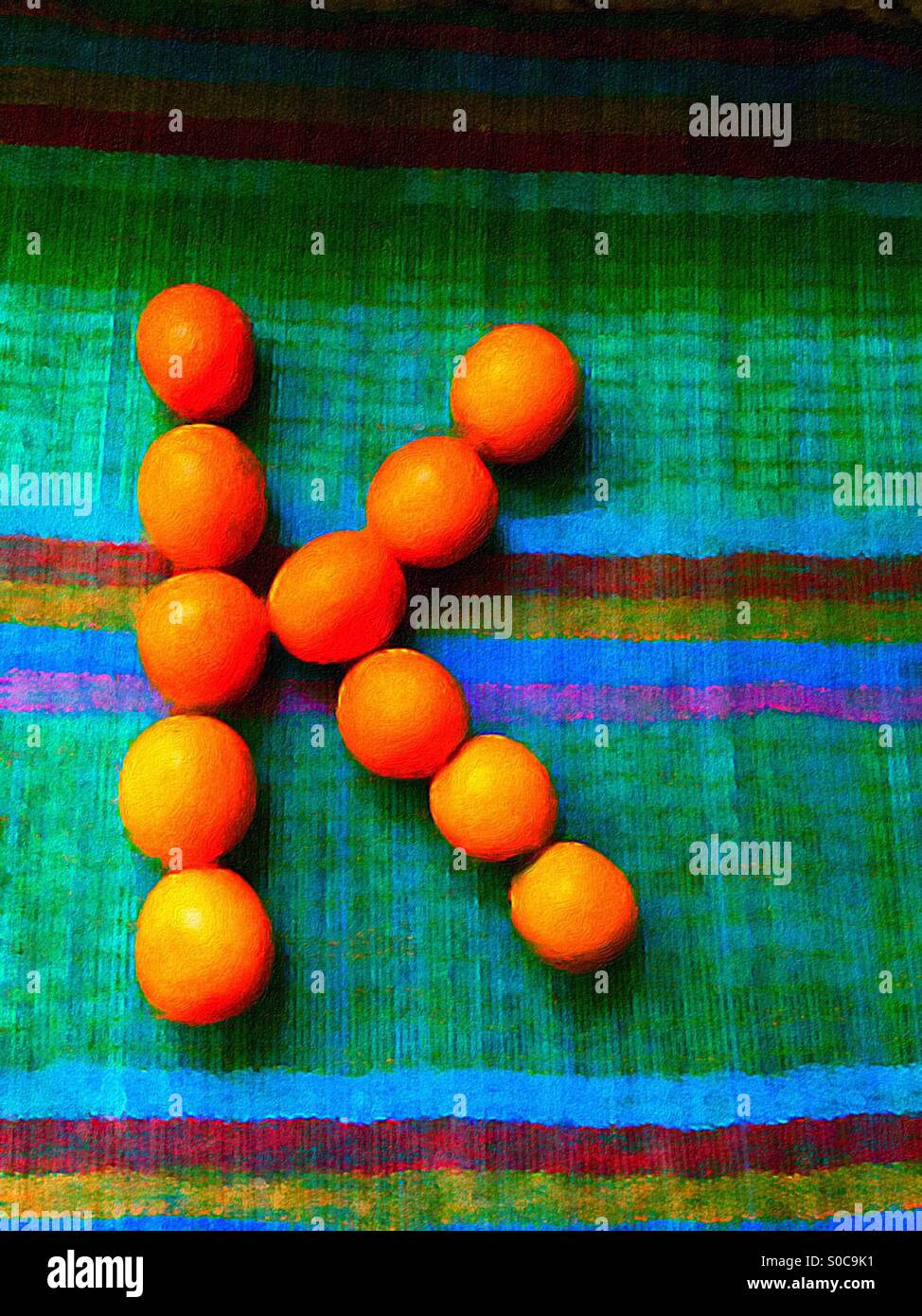 Bemaltes K aus echten, frischen Kumquats auf einer farbenfrohen Bambusmatte. Der Buchstabe K für Kumquat. Kreative Art und Weise des Lernens des Alphabets. Innovative Bildung. Stockfoto