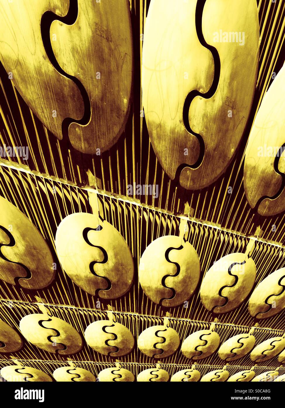 Ein Metalltor mit modernem Design. Vertikale Balken, kreisförmige Formen, wellige, flüssige Linien. Muster wiederholen. Goldene Farbe - Smartphone-aufgenommenes Stockfoto