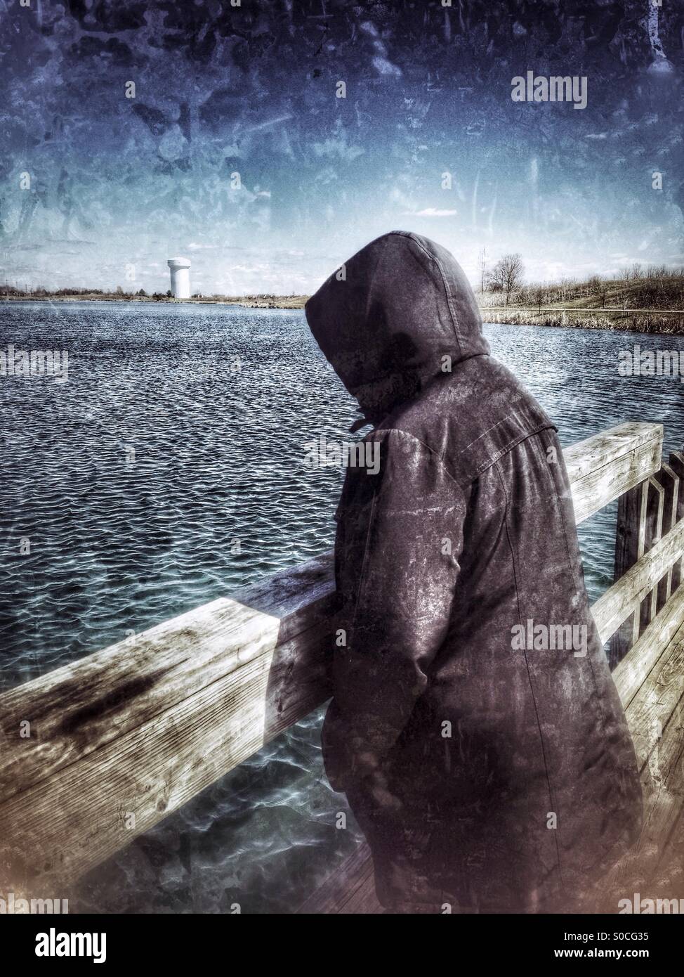 Eine Dame mit einer schwarzen Kapuzen Jacke beobachten die Wellen an einem See (2). Stockfoto