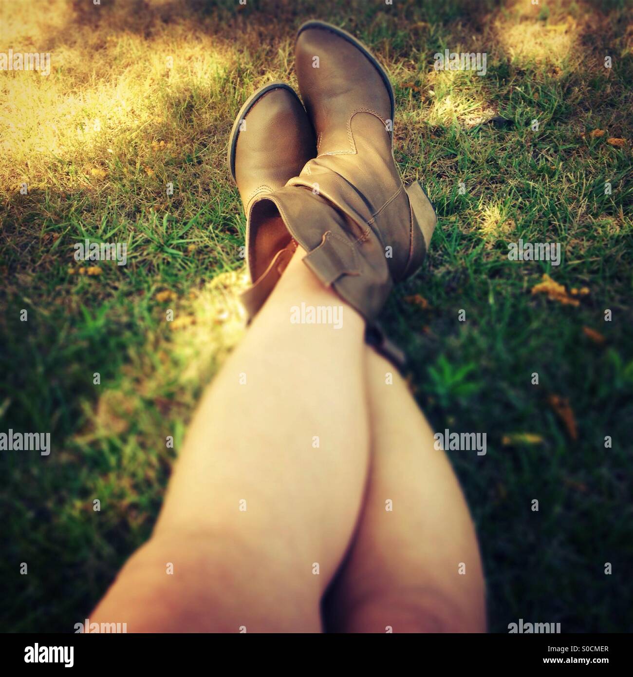 Gekreuzten Beinen auf dem Rasen Cowboy-Stiefeln mit gefleckten Sonnenlicht Stockfoto