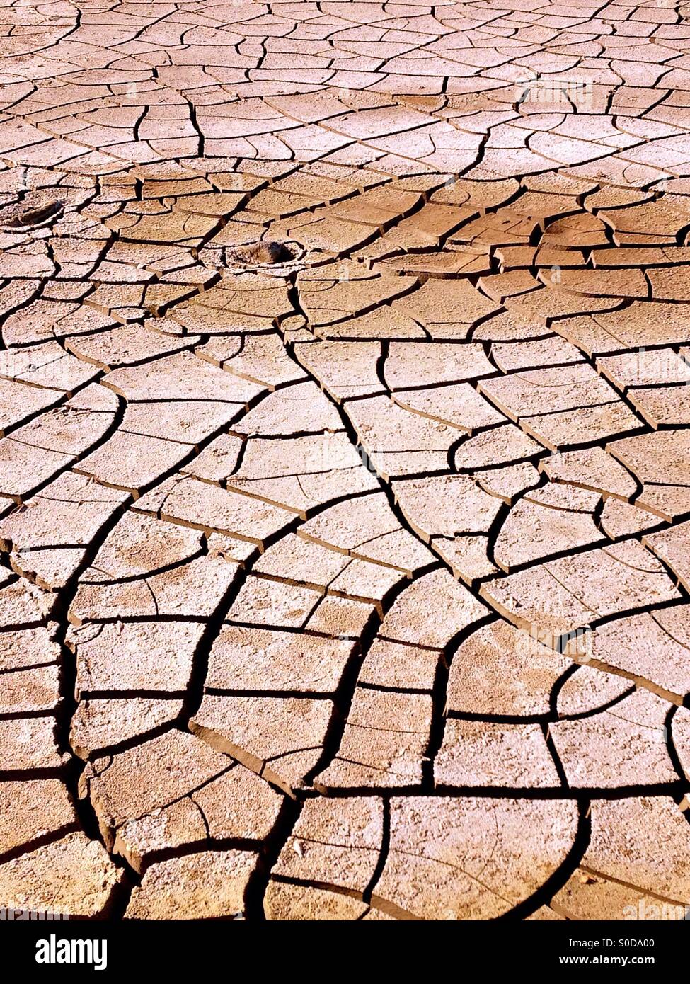 Rissige Erde tritt auf, wenn Wasser aus dem Boden verdunstet. Dies gelingt aride Regionen aufgrund des Fehlens von Wasser oder Dürre Bedingungen. - Smartphone-aufgenommenes Stockfoto