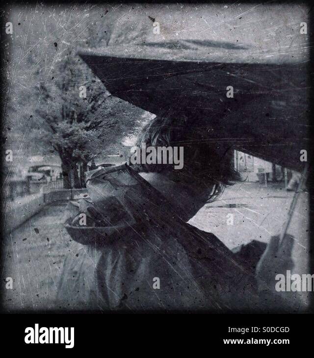 Eine Dame mit Regenschirm bei SMS-Nachrichten auf ihrem Smartphone (Grunge, distressed) überprüfen. - Smartphone-aufgenommenes Stockfoto