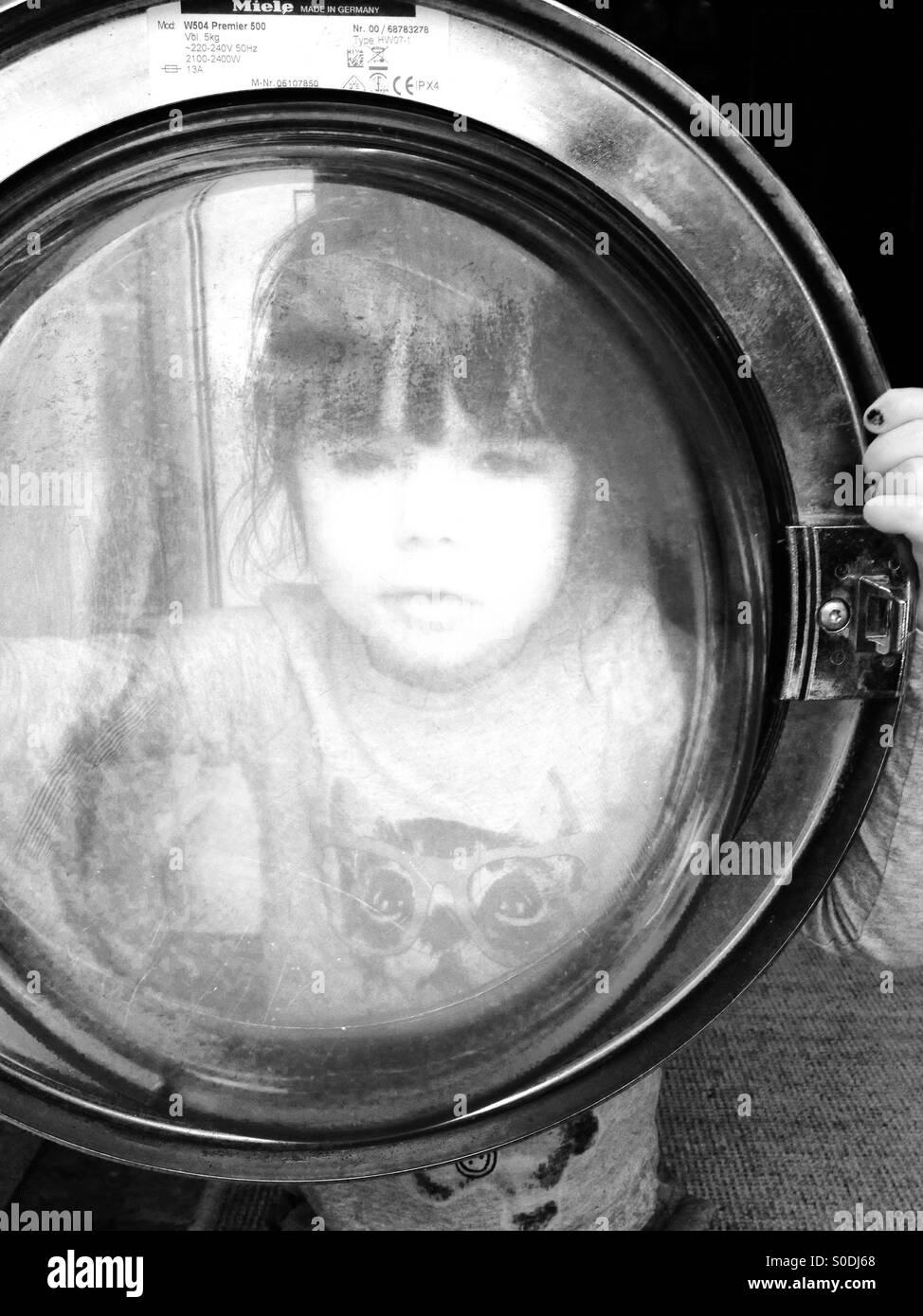 3 - jährige Mädchen auf der Suche durch die Glastür einer Waschmaschine Stockfoto