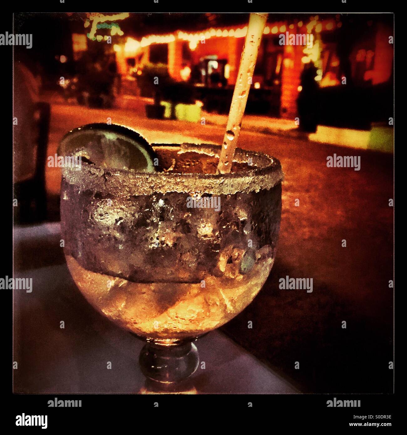 Eine frostige und erfrischende Margarita auf einem Tisch in der Nacht mit den bunten Lichtern ein weiteres Restaurant im Hintergrund auf der Main Street von einem kleinen mexikanischen Pueblo. Stockfoto