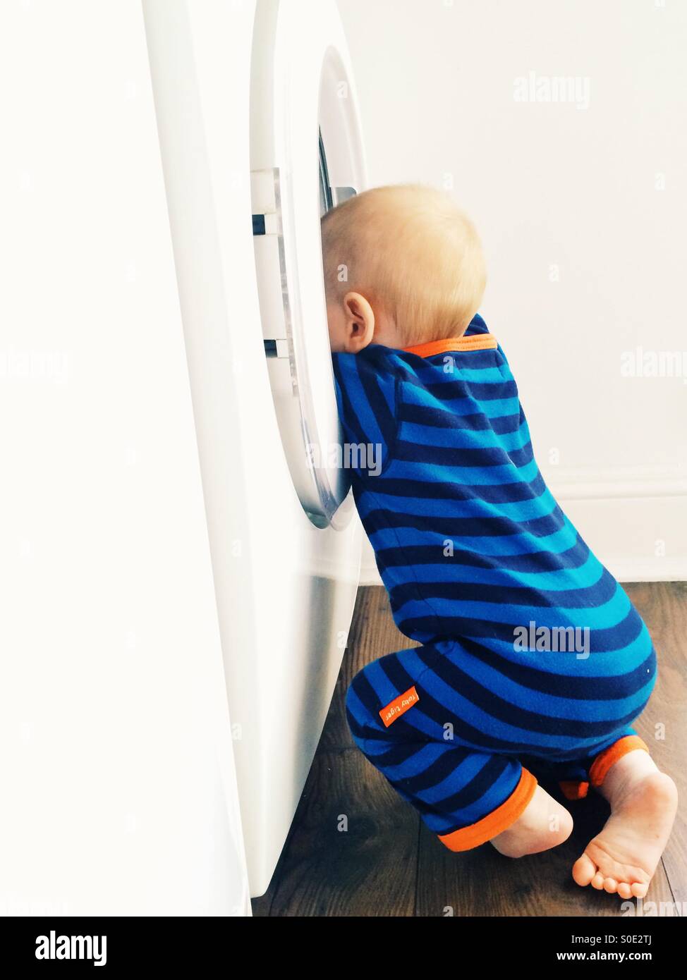 Ein 10 Monate altes Baby junge versucht, in eine Waschmaschine zu klettern Stockfoto