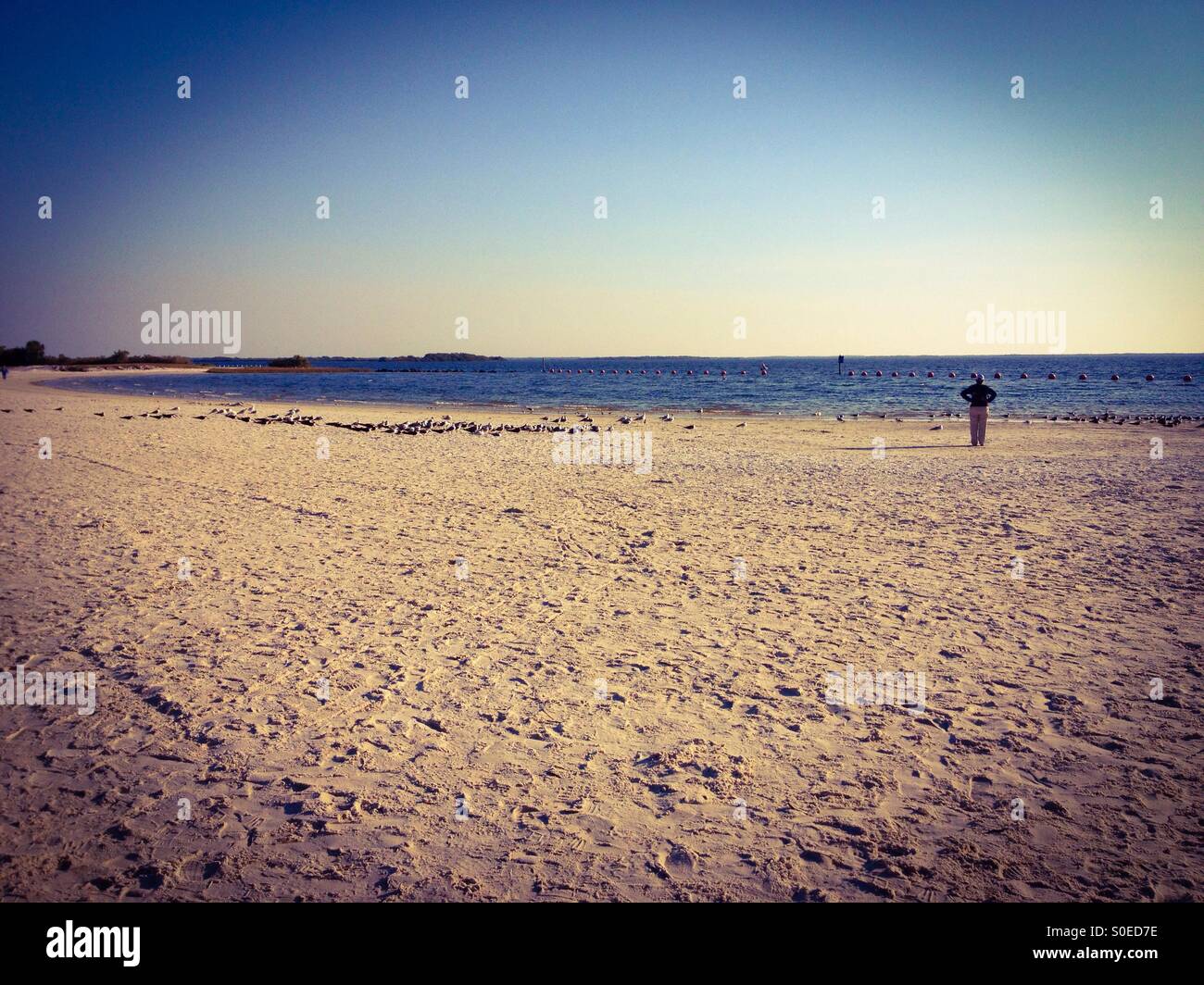 Einsame Figur an einem Sandstrand am Meer. Stockfoto