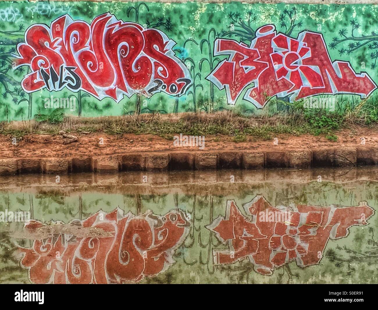 Smaragd Grün und rot Graffiti spiegelt sich wieder in einen Fluss. Stockfoto